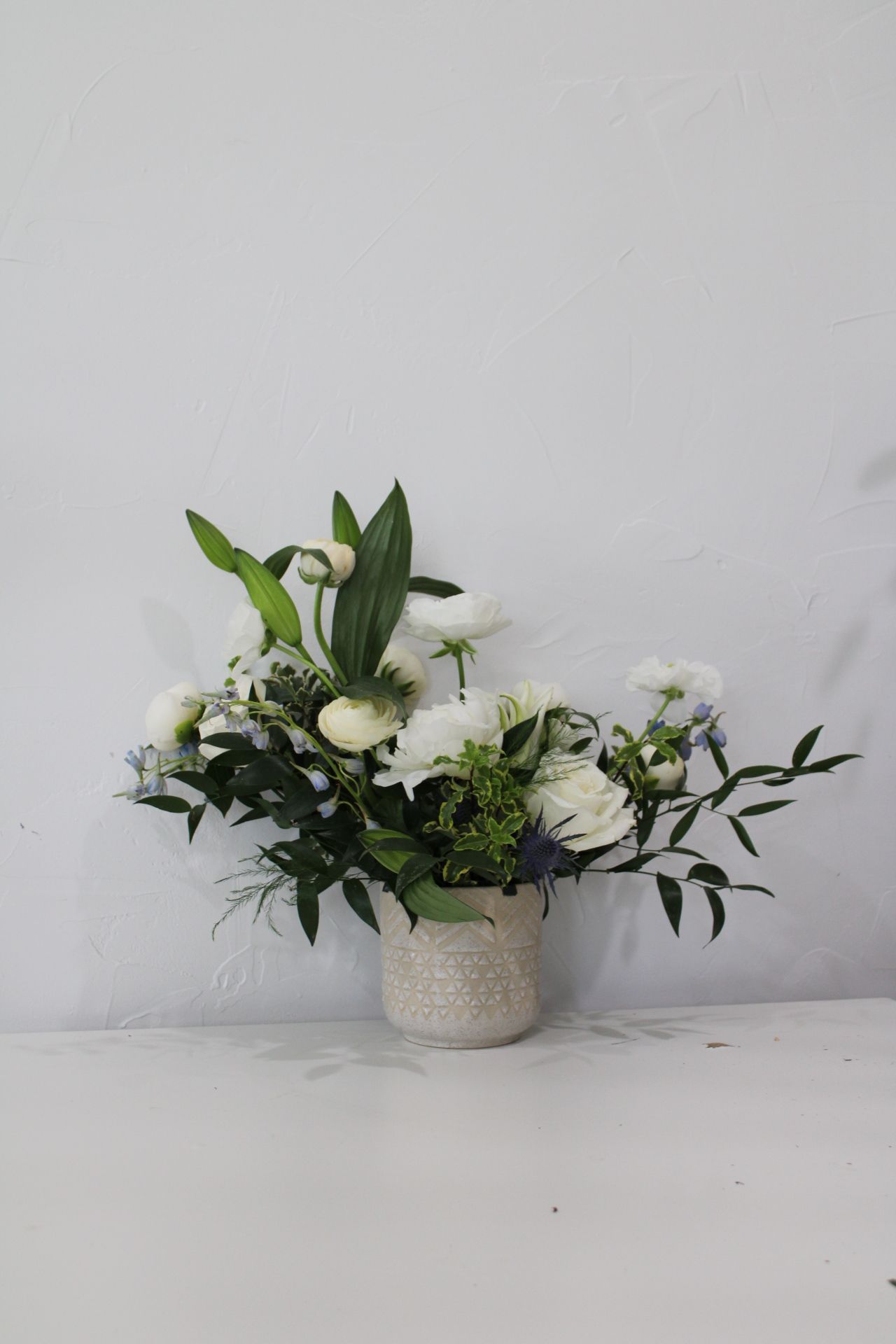 Classic white floral arrangement with lilies and foliage in a textured ceramic vase.
