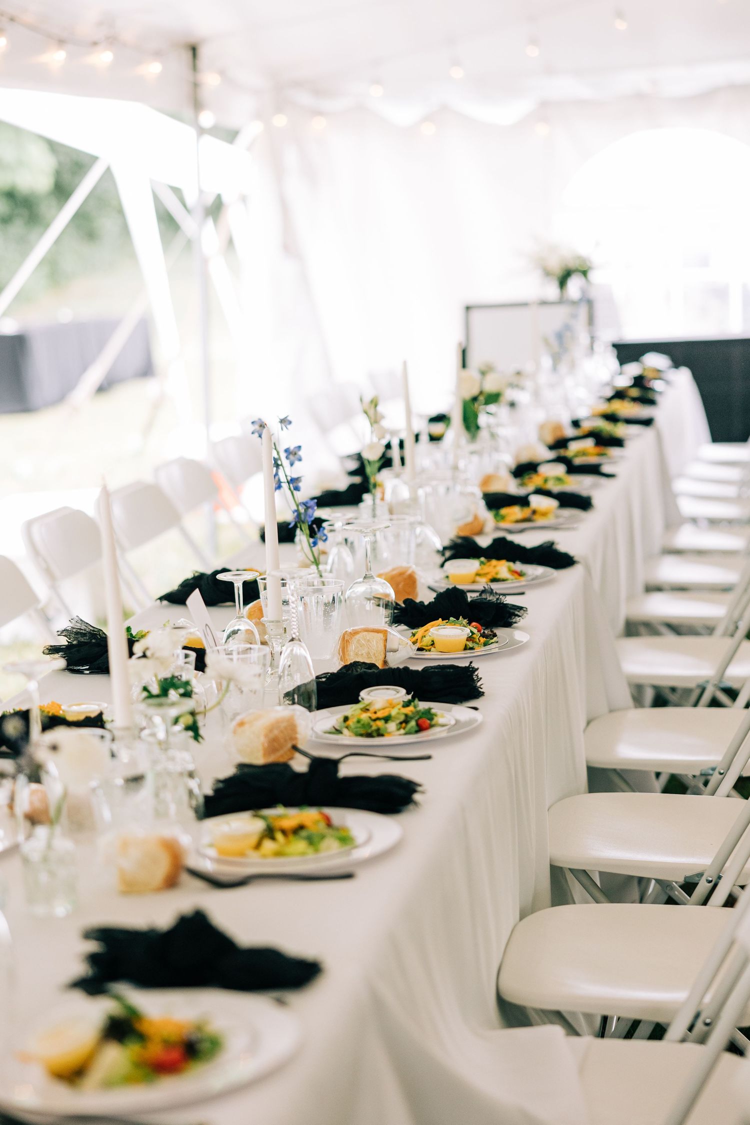Elegant wedding reception table with white linens, black napkins and plated meals set for dinner service.