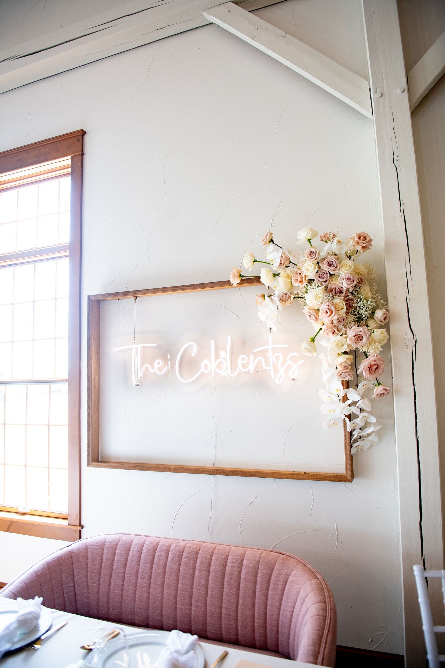 Neon sign reading 'Two Celebrate' with pink floral accents and pink velvet seating.