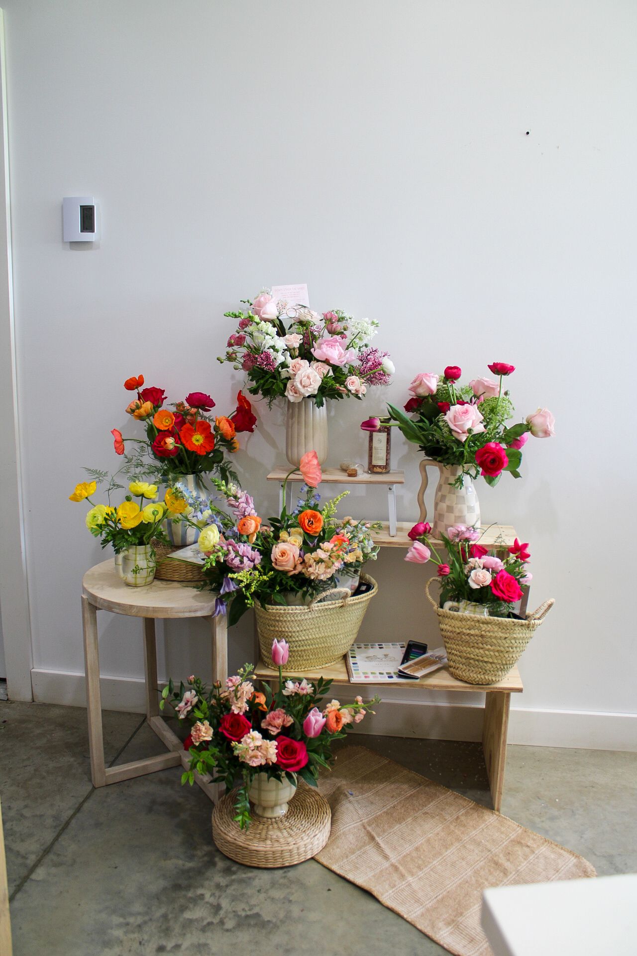 Colorful floral arrangements in wicker baskets and vases displayed on wooden benches in a bright flower shop.