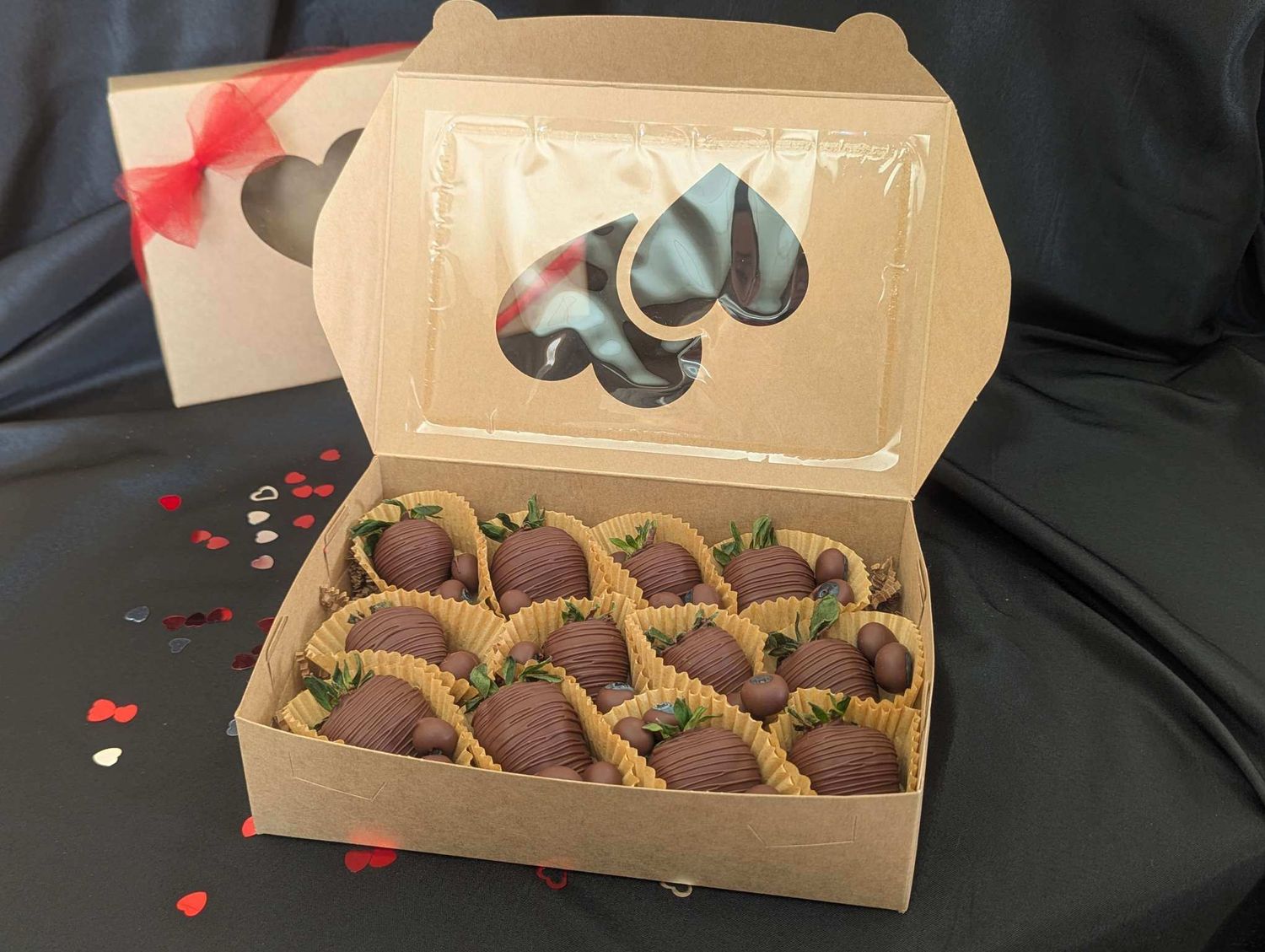 Box of handmade chocolate truffles with gold decorative accents displayed on dark fabric with red heart decorations.