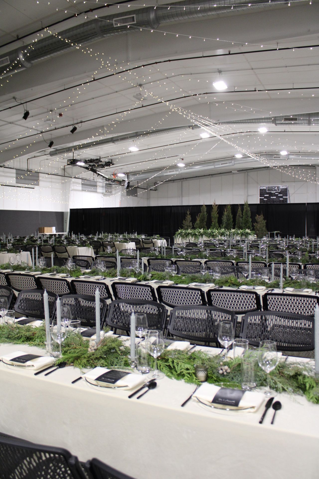 Long banquet table set with elegant black chairs, white tablecloths, and glassware in a modern event space.