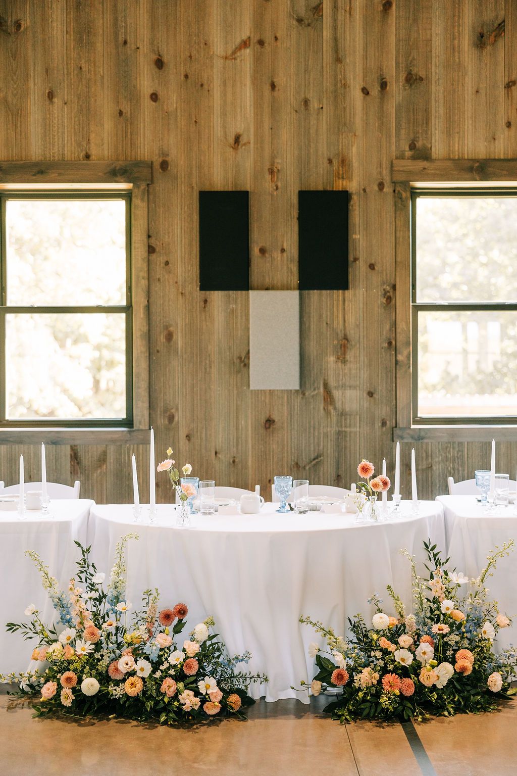 Long banquet table adorned with elegant floral arrangements and white linens in a rustic wooden barn setting.