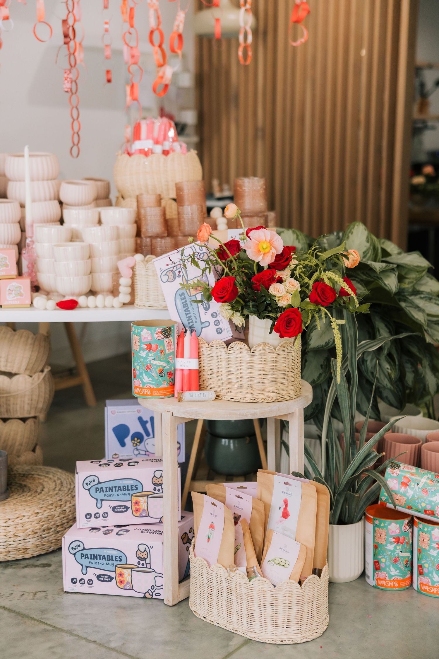 Elegant party setup with pink decorations, white candles, red roses, and woven baskets arranged on wooden tables.