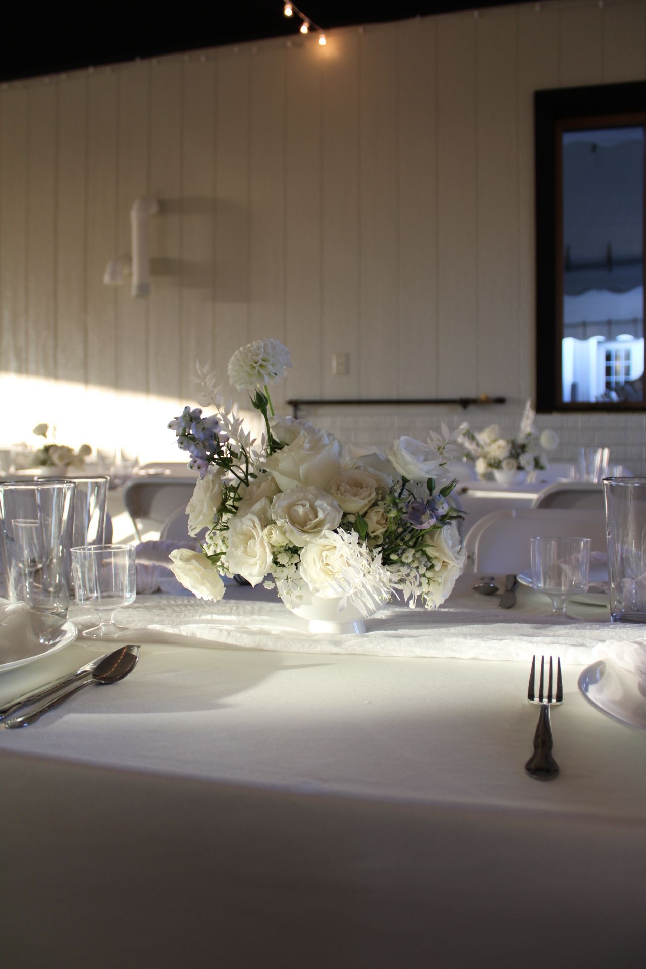 Elegant white floral centerpiece on a formal dining table with crystal glassware and place settings.
