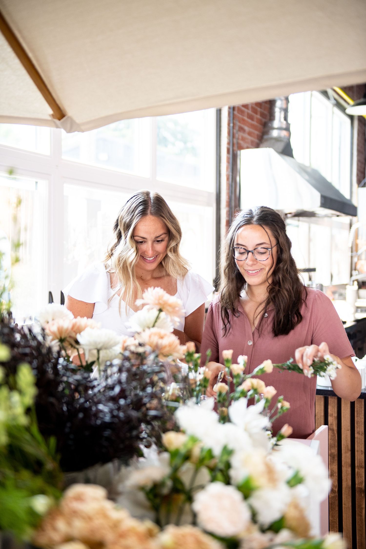 People arranging fresh flowers at an indoor market stall with natural lighting.