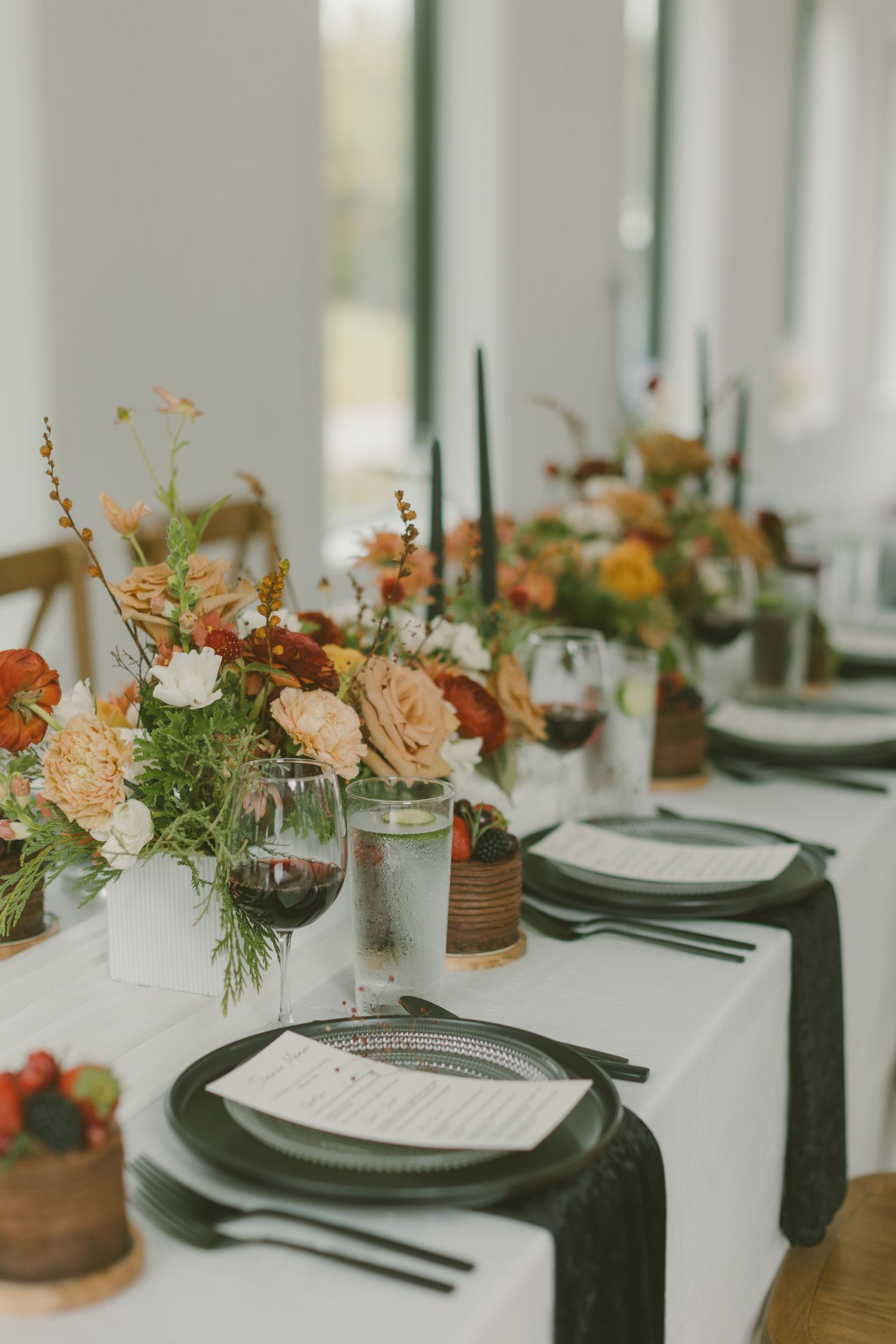 Modern tablescape with dark charger plates, linen napkins, and peach floral centerpieces.