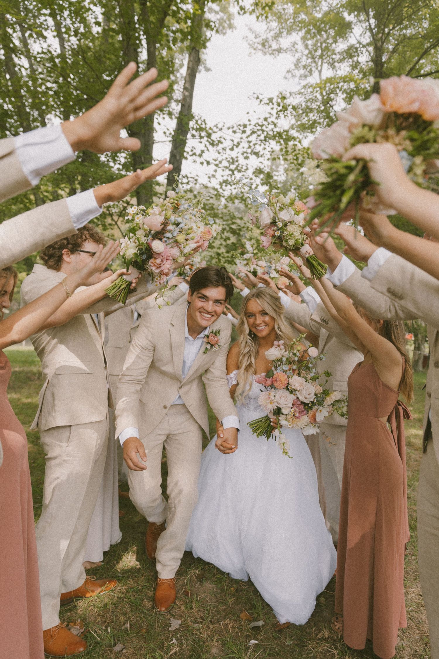 Wedding party celebrates with raised hands in a joyful outdoor moment.