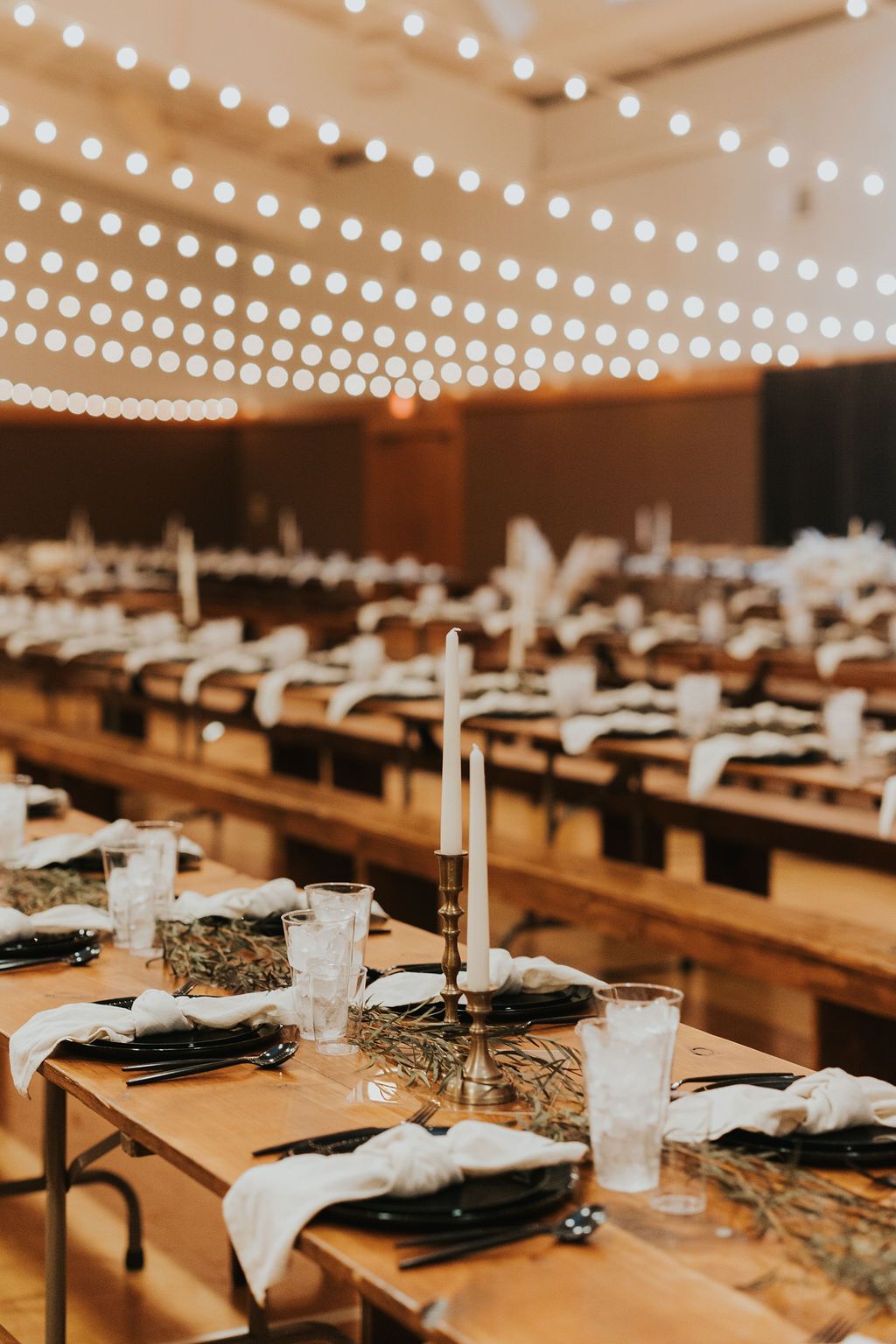 Rustic wedding reception setup with wooden tables, black plates, and twinkling string lights creating an intimate atmosphere.