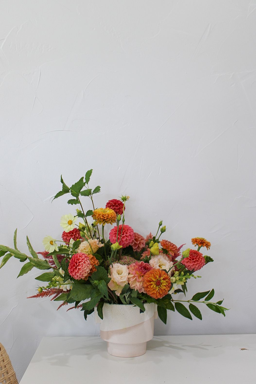Cheerful coral and peach floral arrangement with dahlias and roses in a modern white ceramic vase.