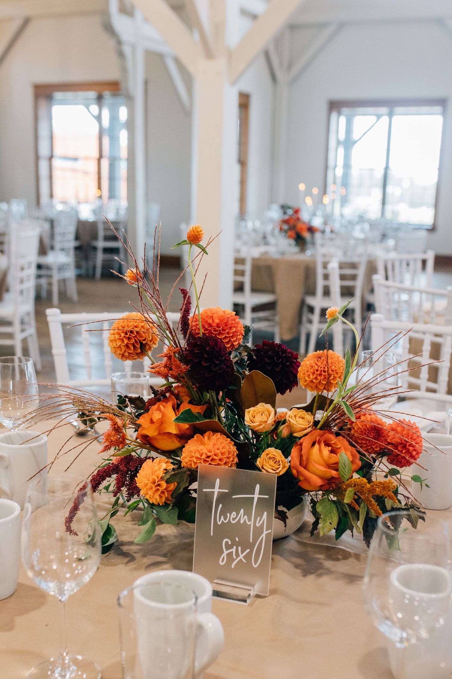 Autumn-inspired centerpiece with orange dahlias and roses on reception table with place card.