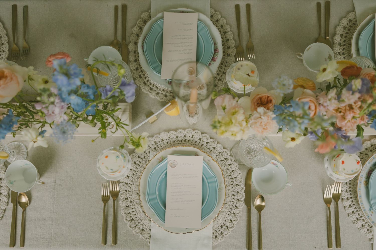Wedding table settings with delicate blue plates and pastel floral arrangements in a formal dining setup.
