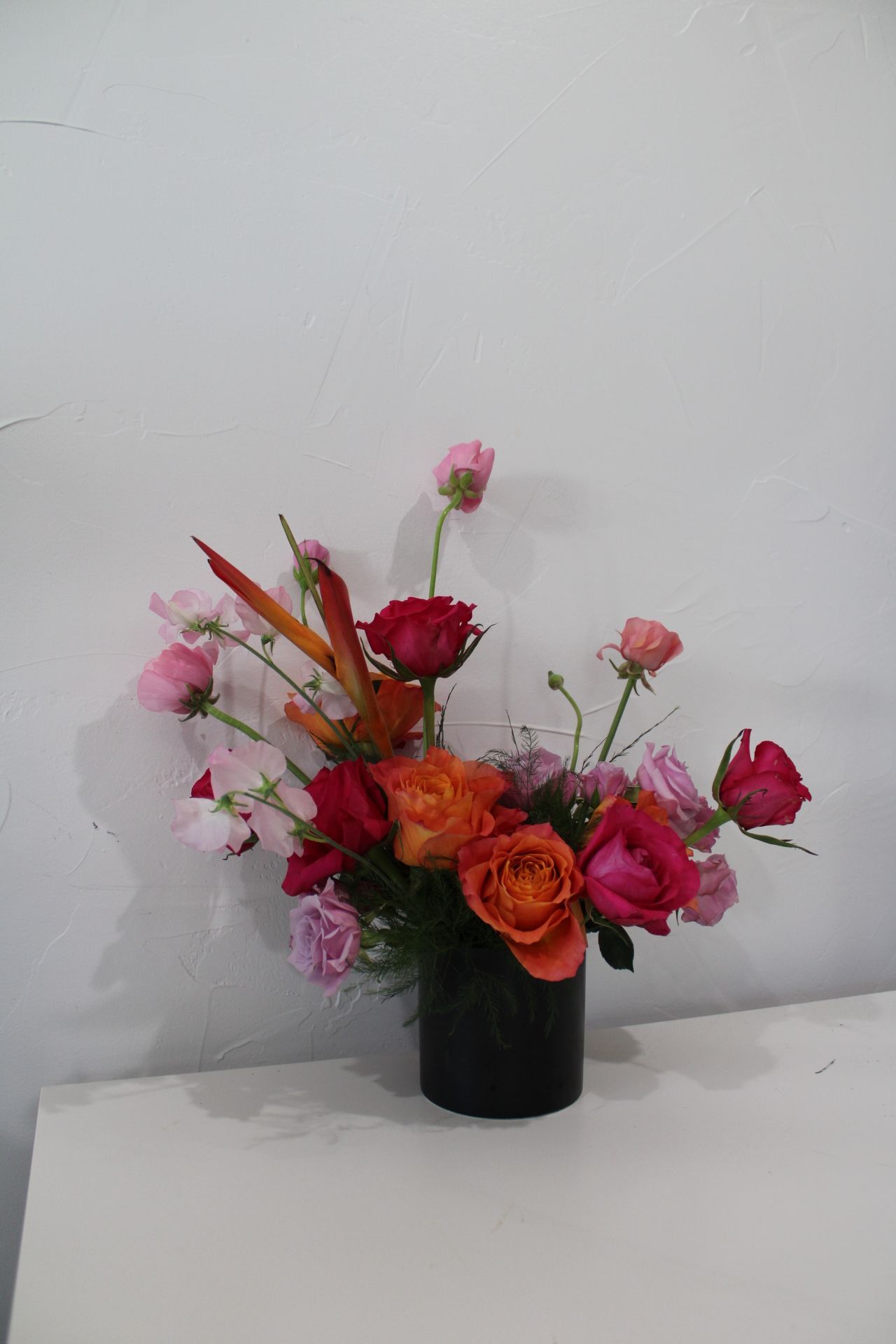 Bold arrangement of pink and red roses with orange accents in black modern vase.
