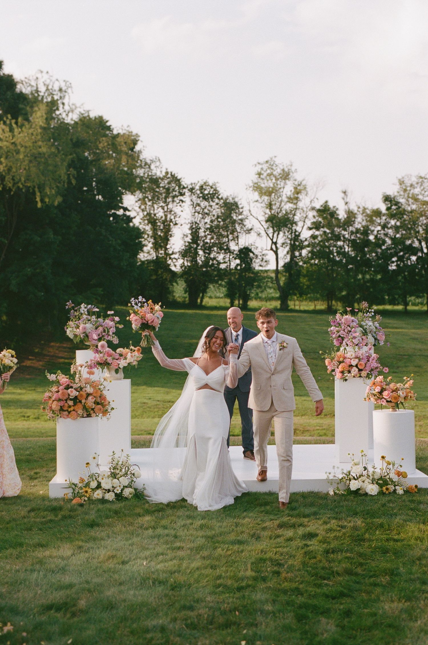 Wedding ceremony site with white columns and pink floral arrangements on grassy lawn.