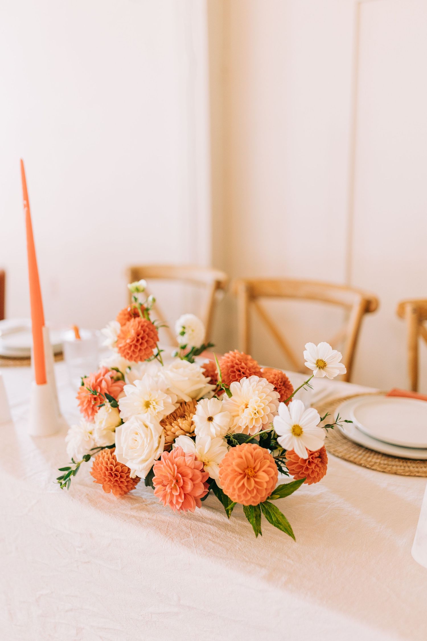 Coral and white floral centerpiece with dahlias and roses on white linen tablecloth.