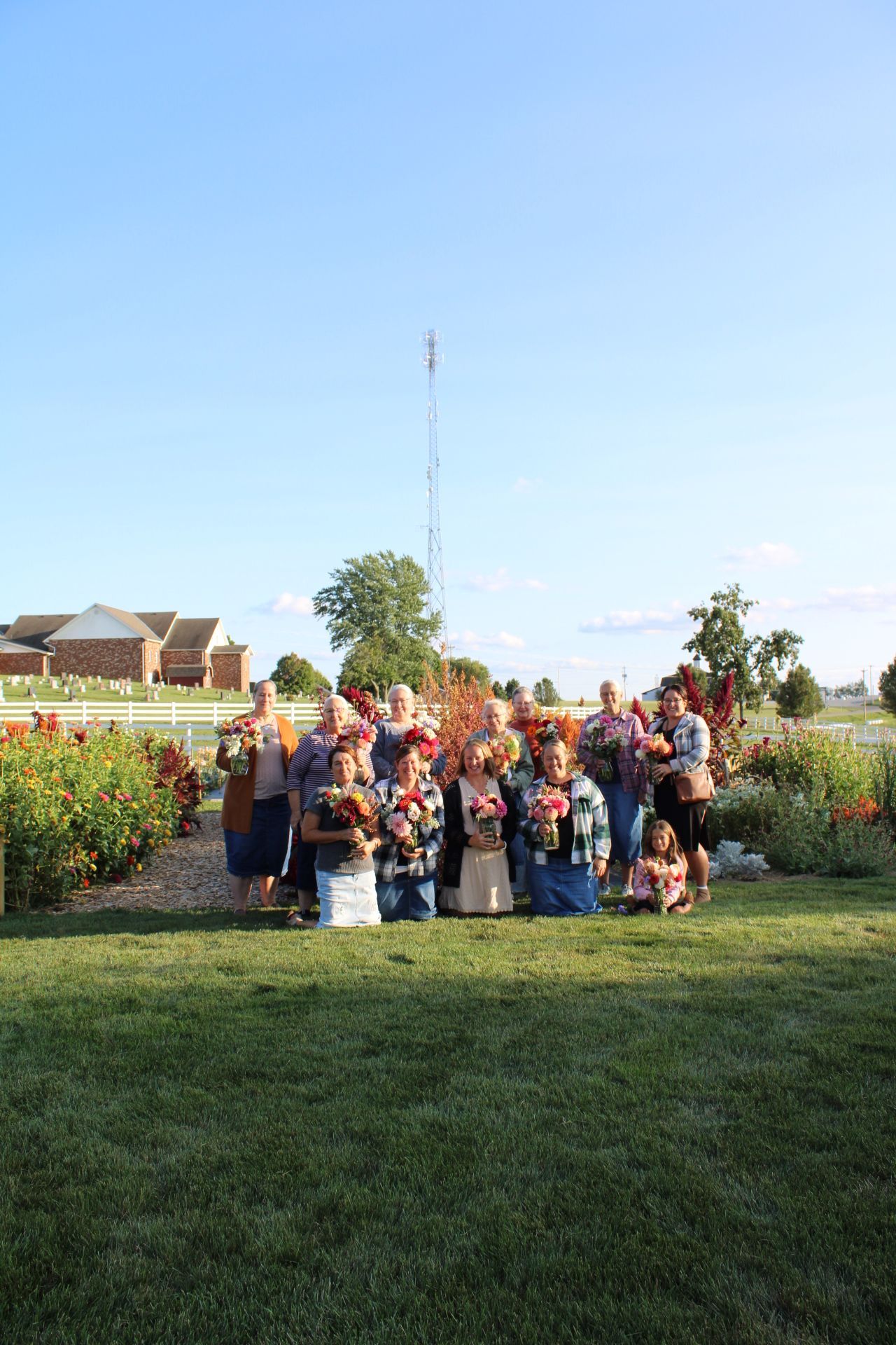 Large group gathered outdoors in a garden setting with a communications tower visible in the background.