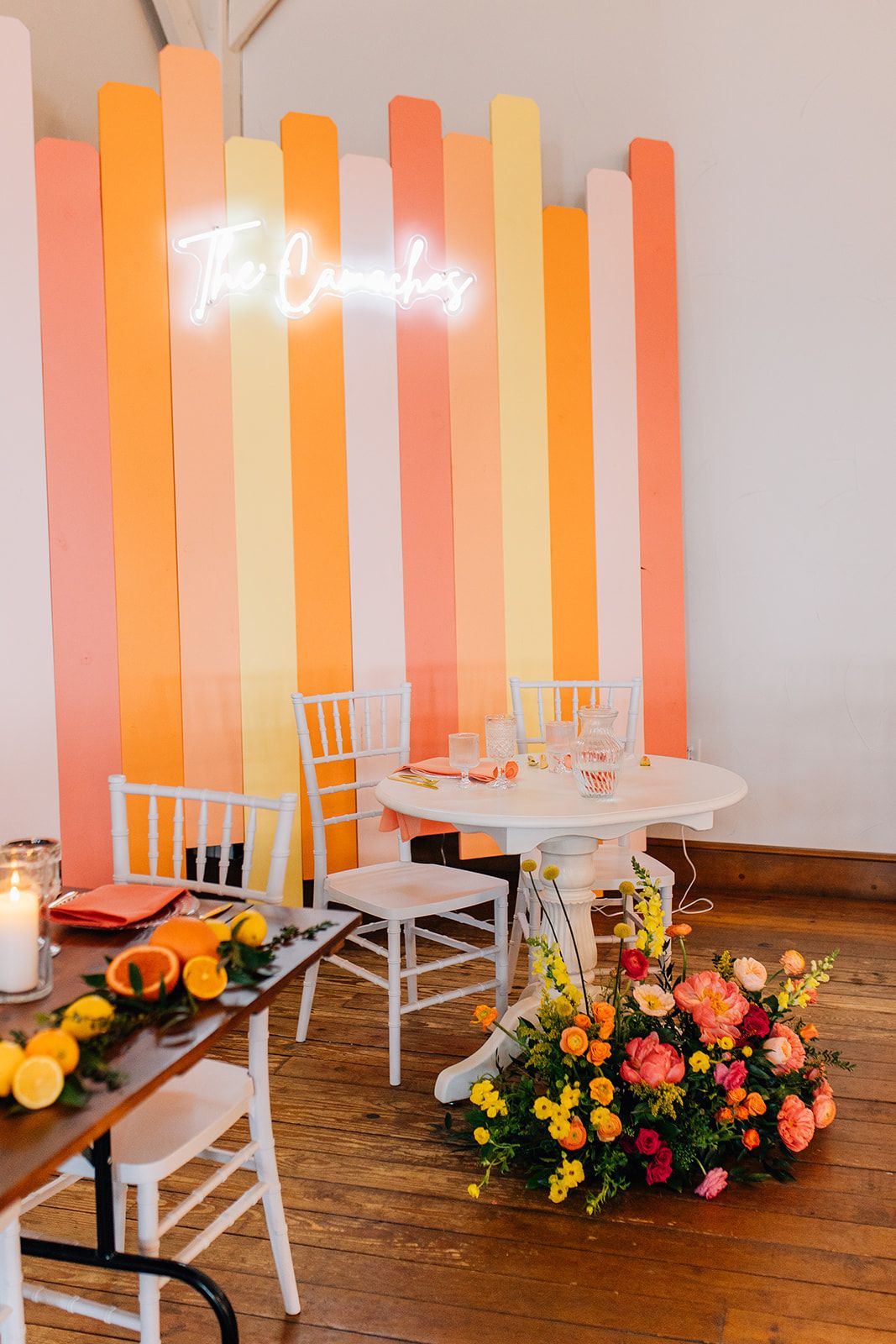 Modern event space with orange and white striped walls, white chairs, round tables and colorful floral arrangements.