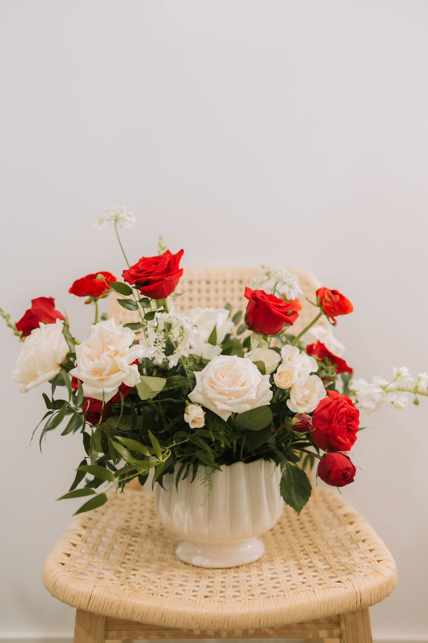 Elegant floral arrangement with red and white roses in a white ceramic vase displayed on a woven rattan table.