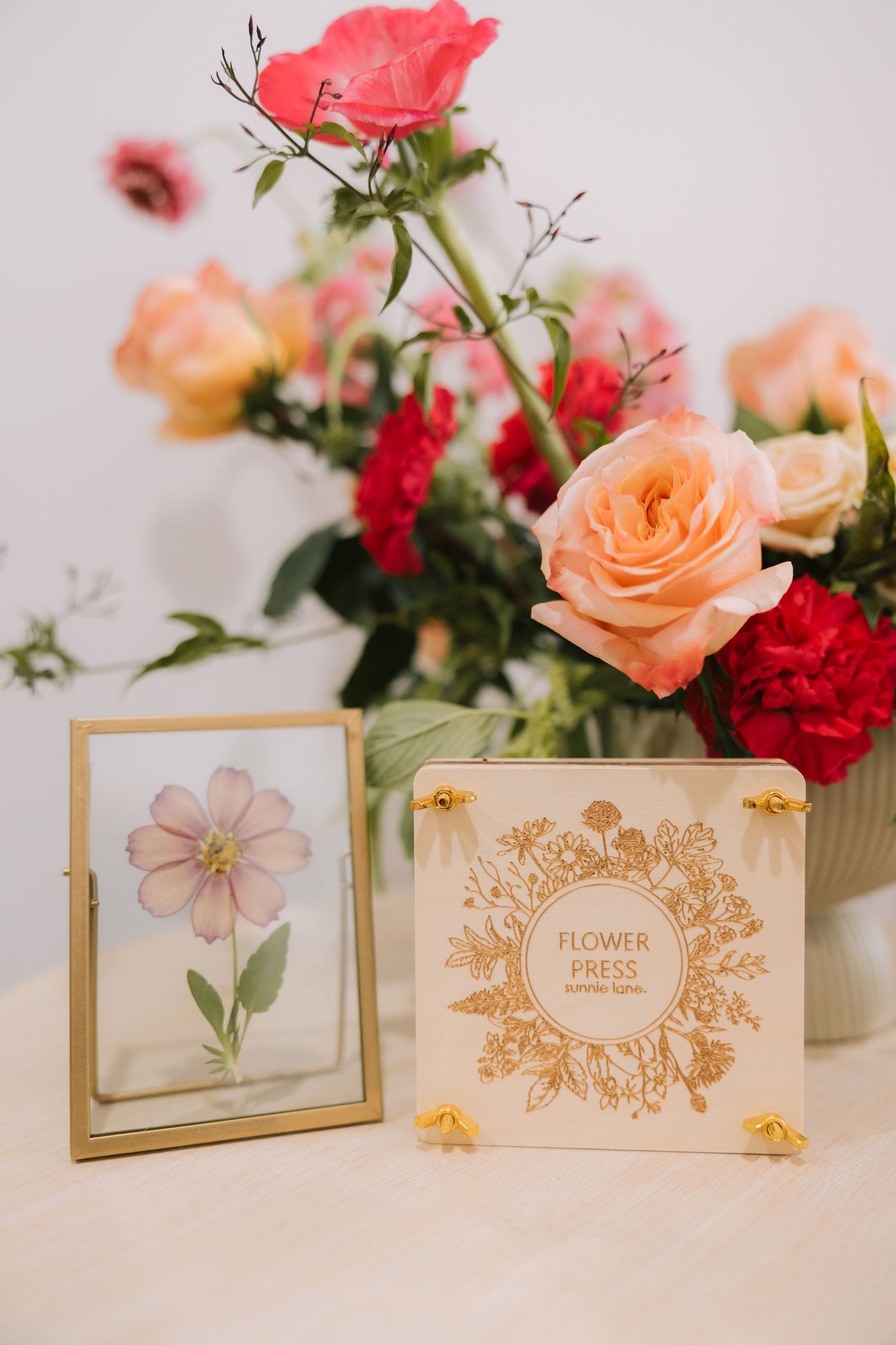 Elegant floral arrangement with coral and red roses alongside framed flower artwork and gold-detailed press book.