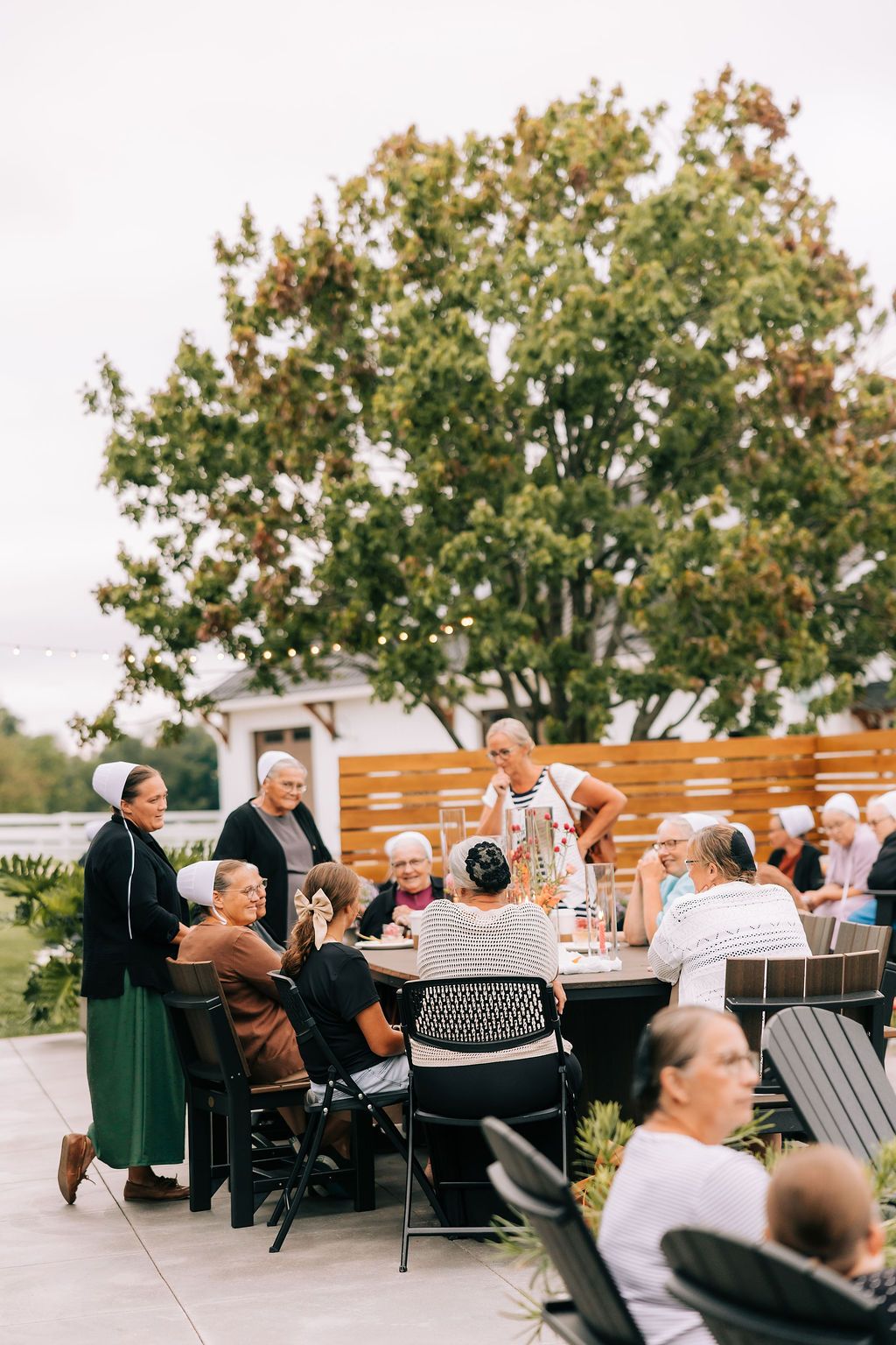 People enjoying a casual outdoor dining experience at tables arranged on a patio with trees in the background.