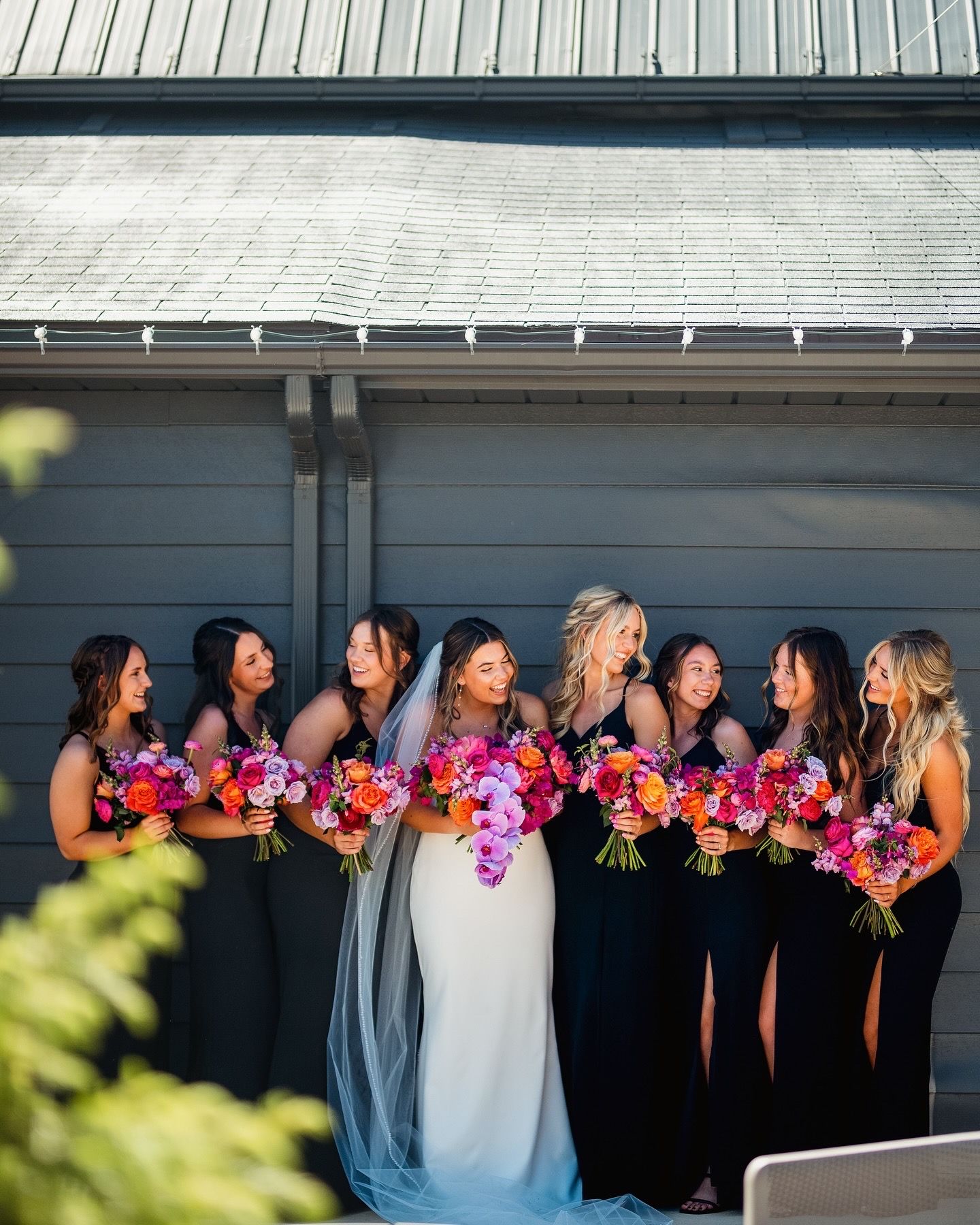 Wedding party posing against modern building with vibrant pink and purple bouquets.