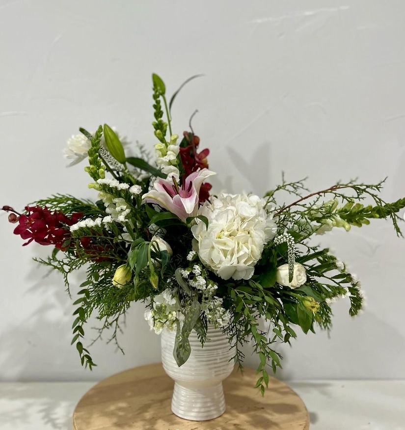 White and burgundy floral centerpiece with greenery in textured ceramic vase.