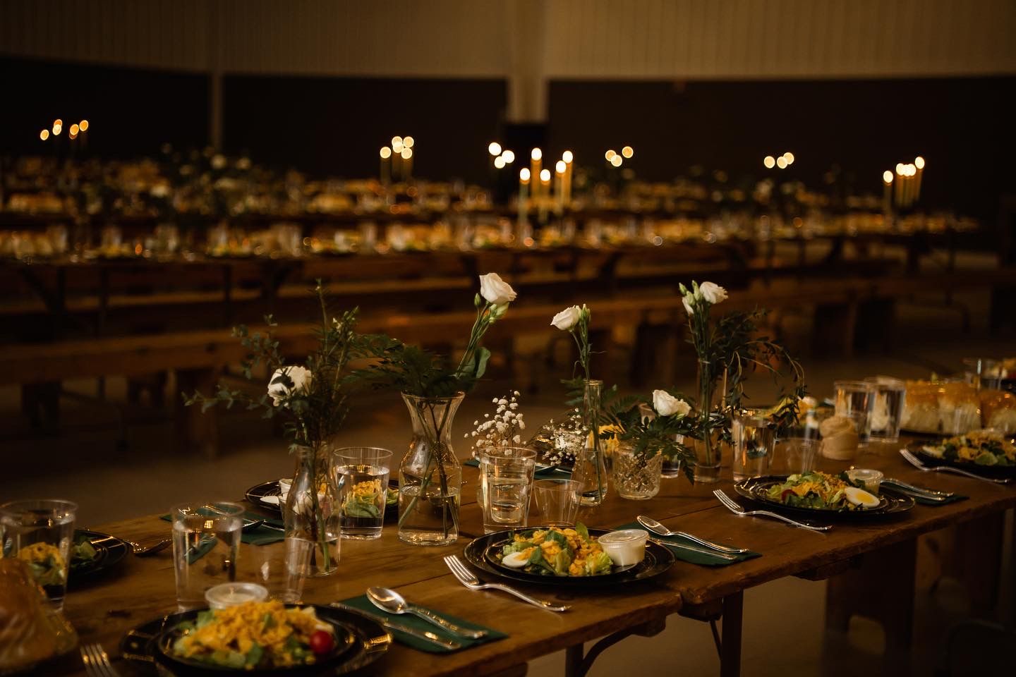 Intimate table settings with glowing candles and delicate floral arrangements in a darkened reception space.