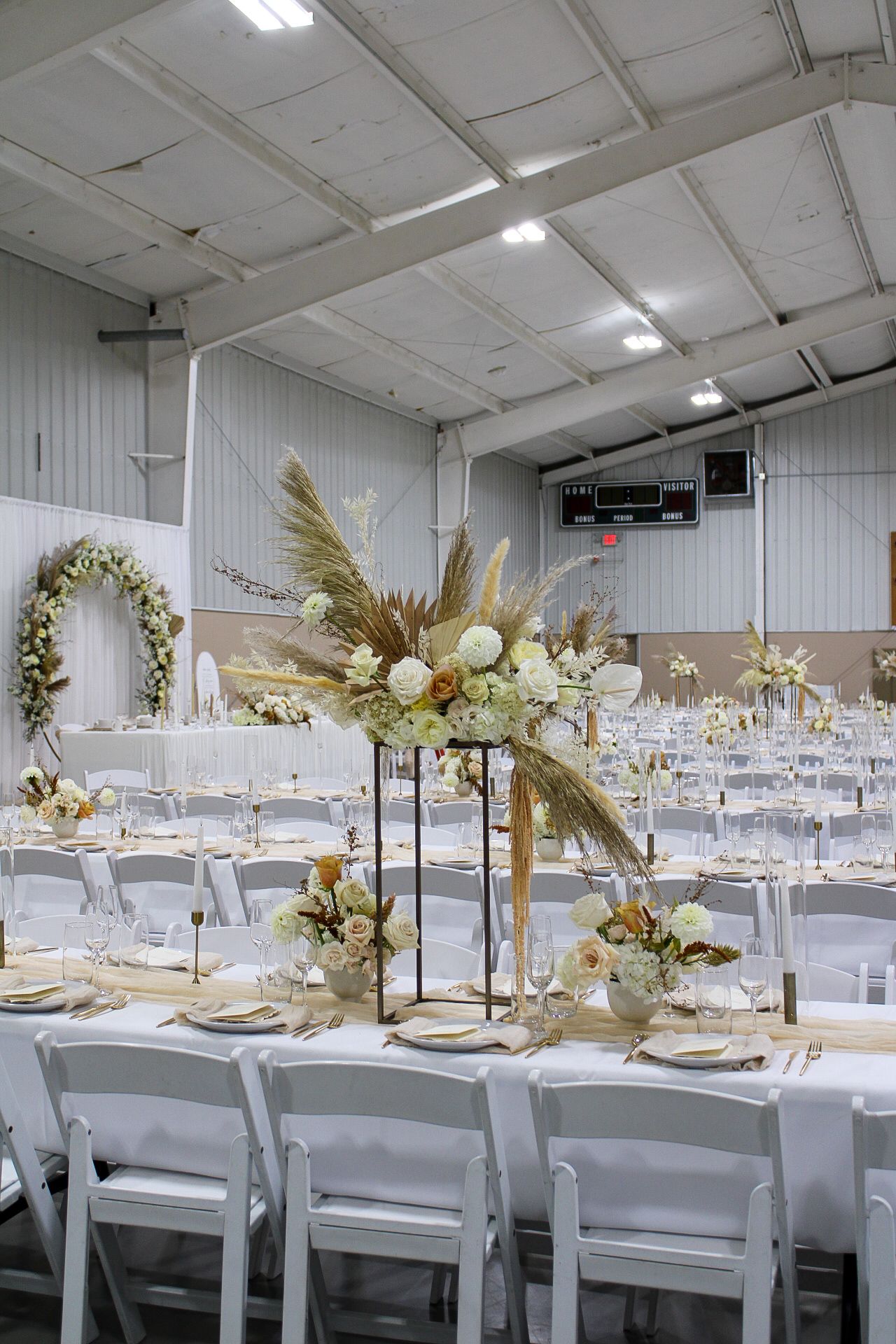 Elegant wedding reception tables decorated with dried pampas grass and floral arrangements in a white industrial venue.