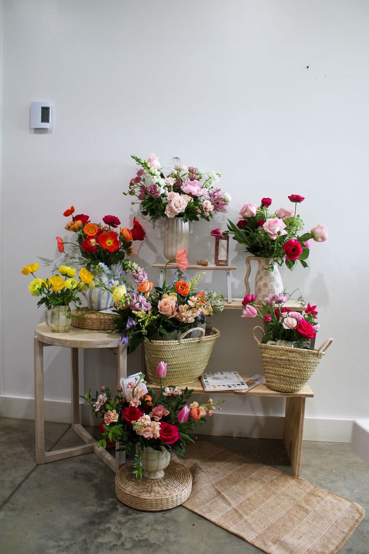 Colorful flower arrangements in baskets and vases displayed on wooden tables in a bright floral shop.