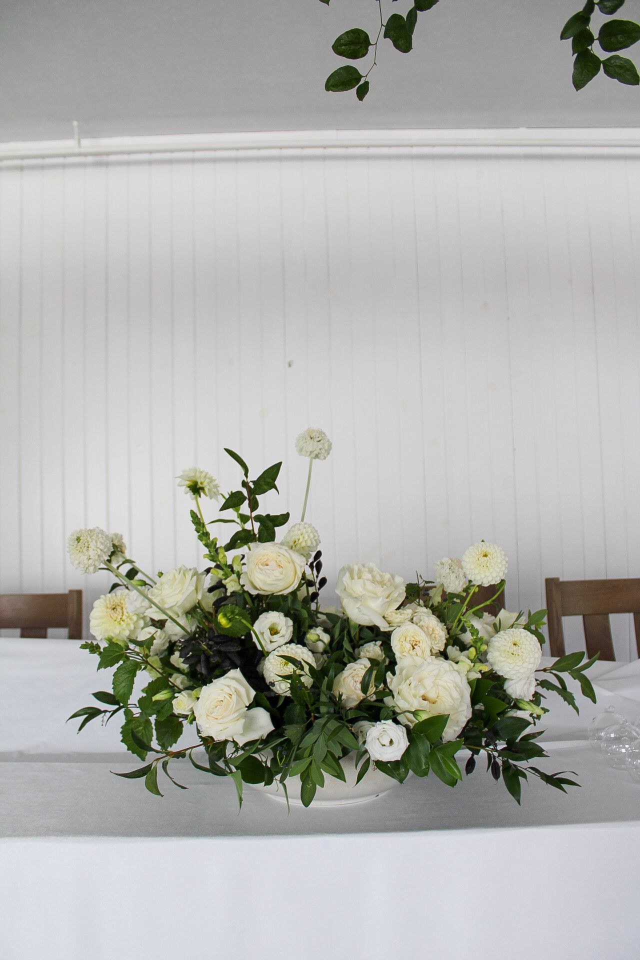 Elegant white rose and greenery centerpiece on crisp white tablecloth.