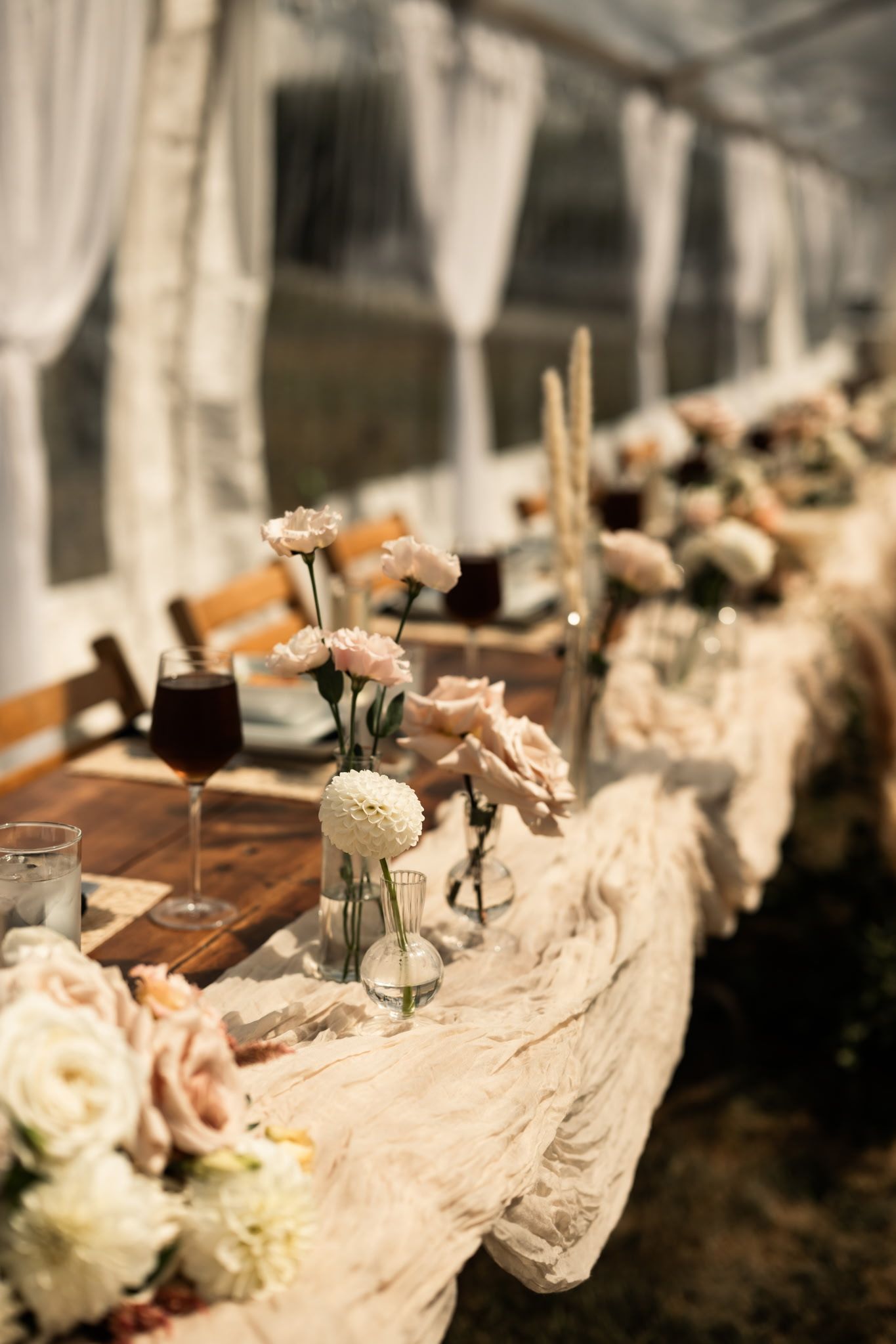 Rustic wedding table decorated with roses in glass vases and flowing fabric runners.
