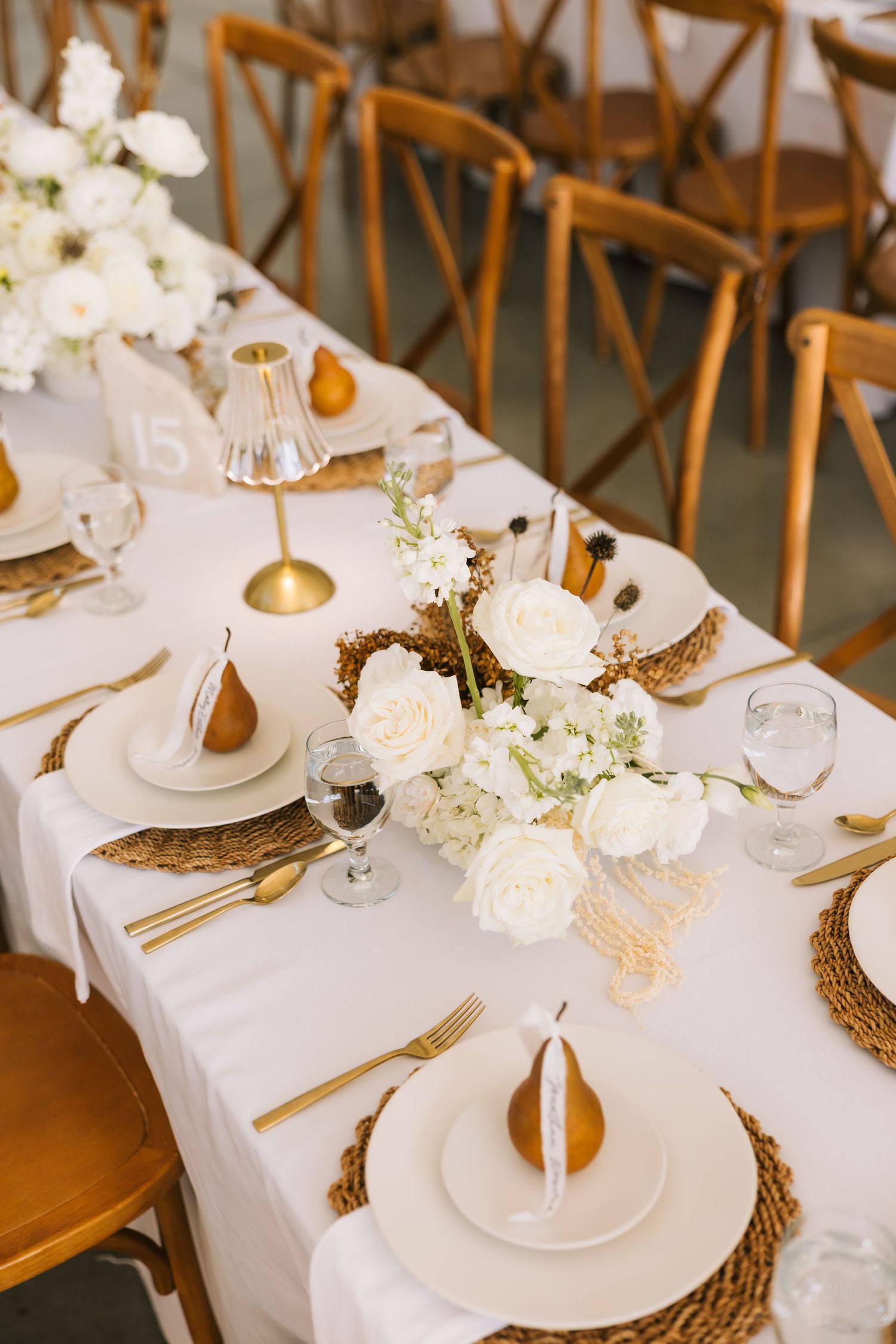 Elegant wedding table setting with white linens, woven chargers, gold flatware and delicate floral centerpieces.