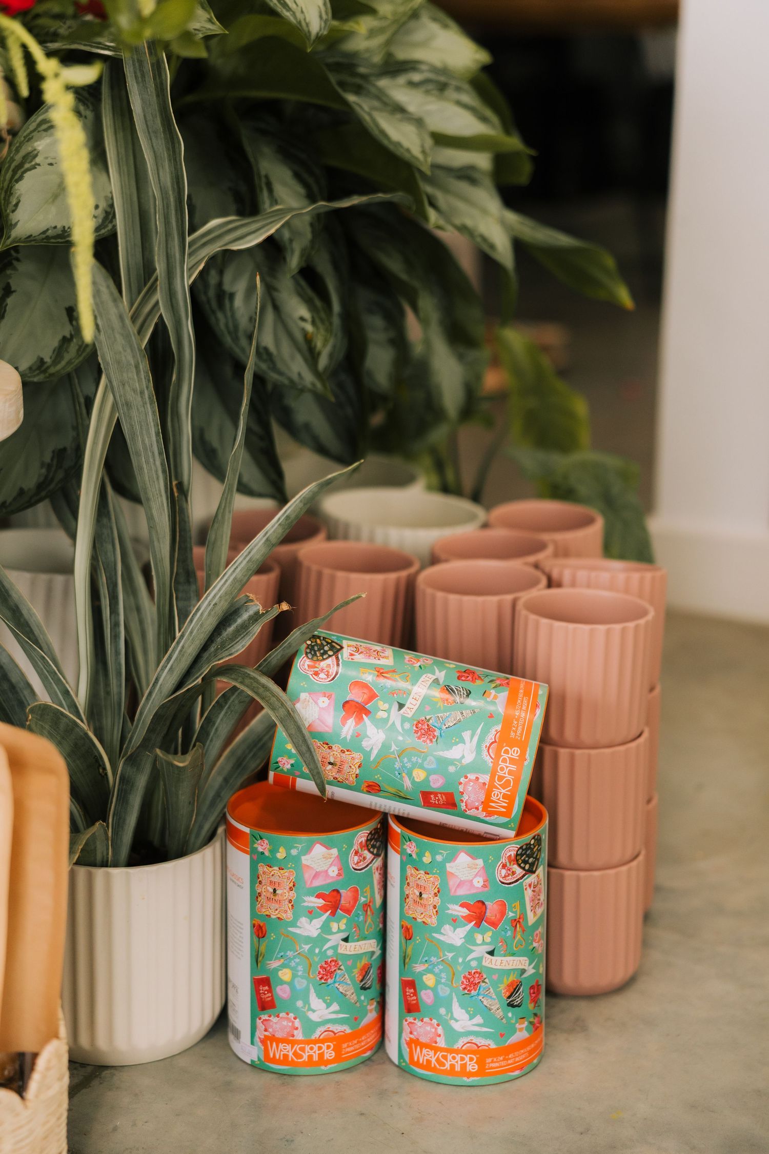 Decorative ceramic planters in pink and floral patterns arranged beside green plants on a concrete surface.