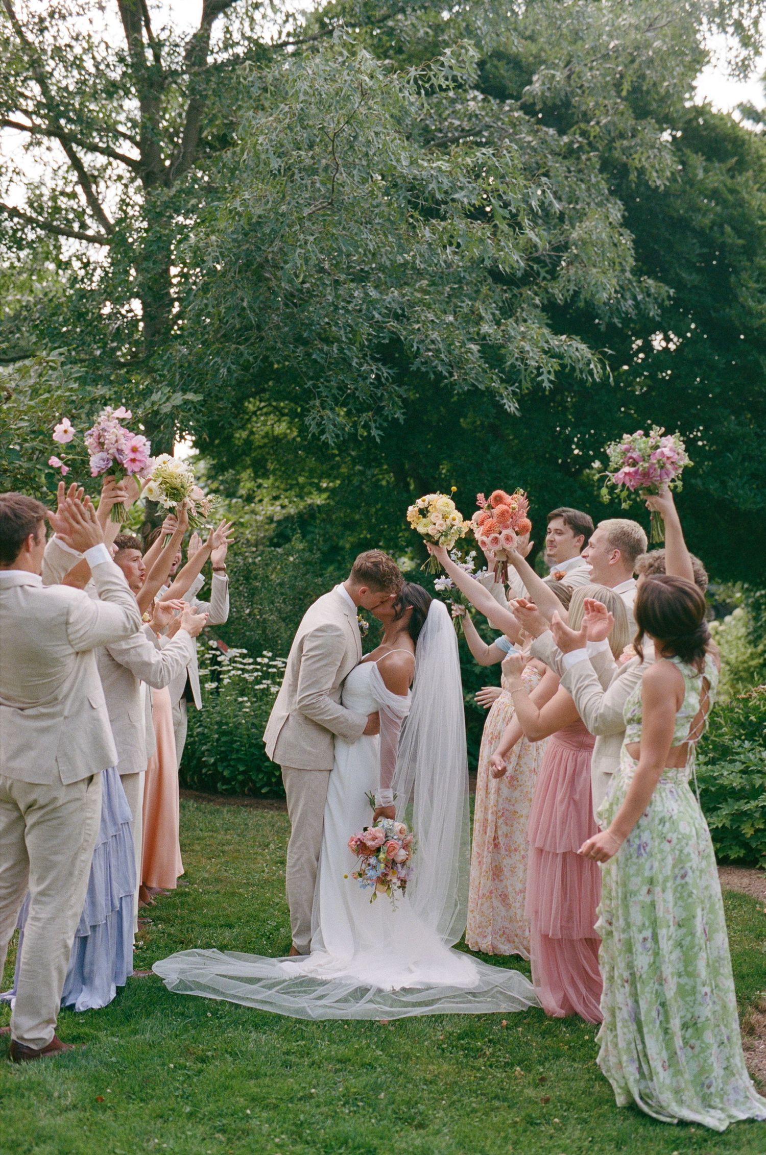 Wedding ceremony in a garden setting with bridal party holding bouquets overhead.