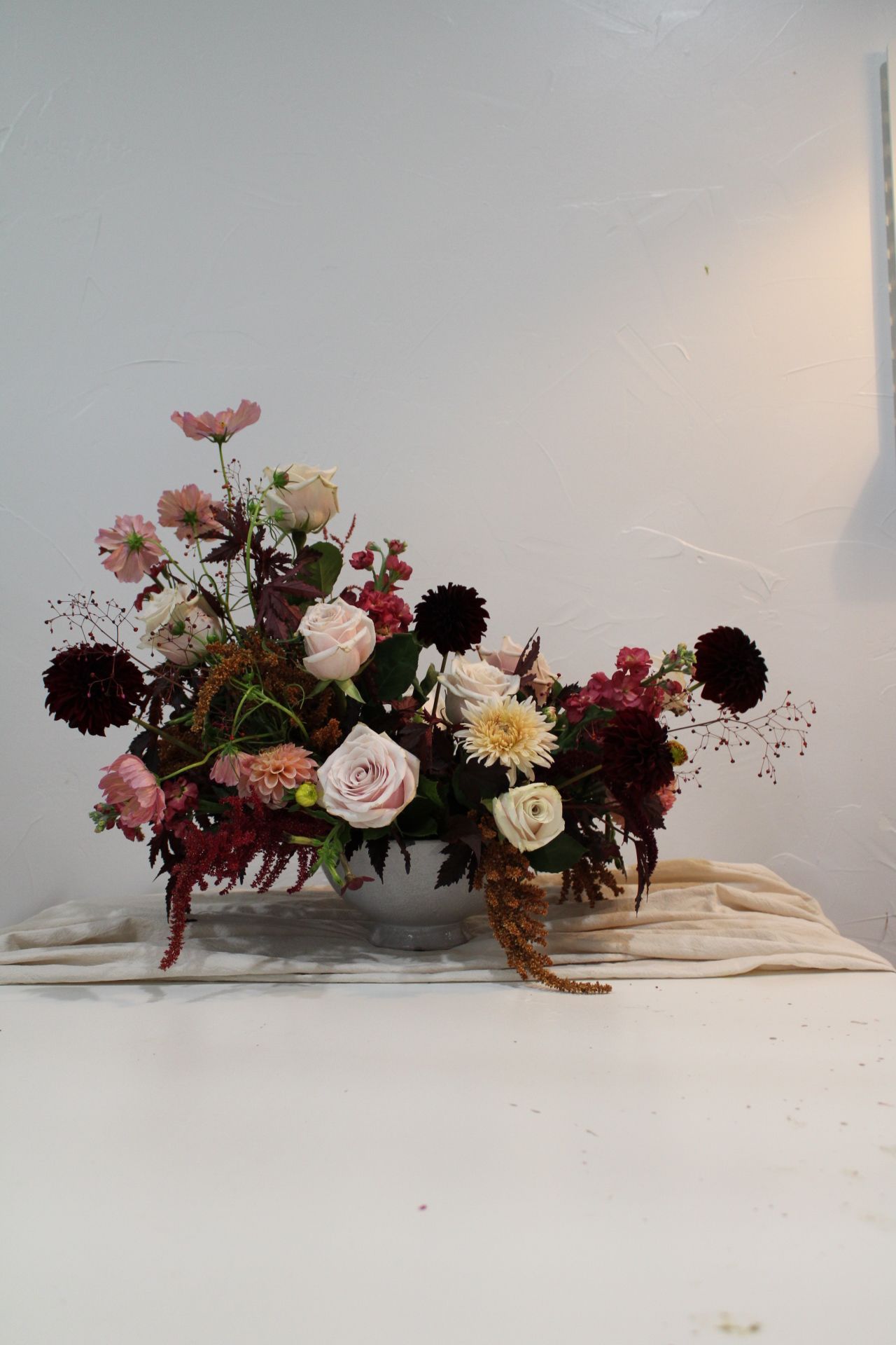 Moody floral arrangement with burgundy and blush blooms in dark tones against white background.