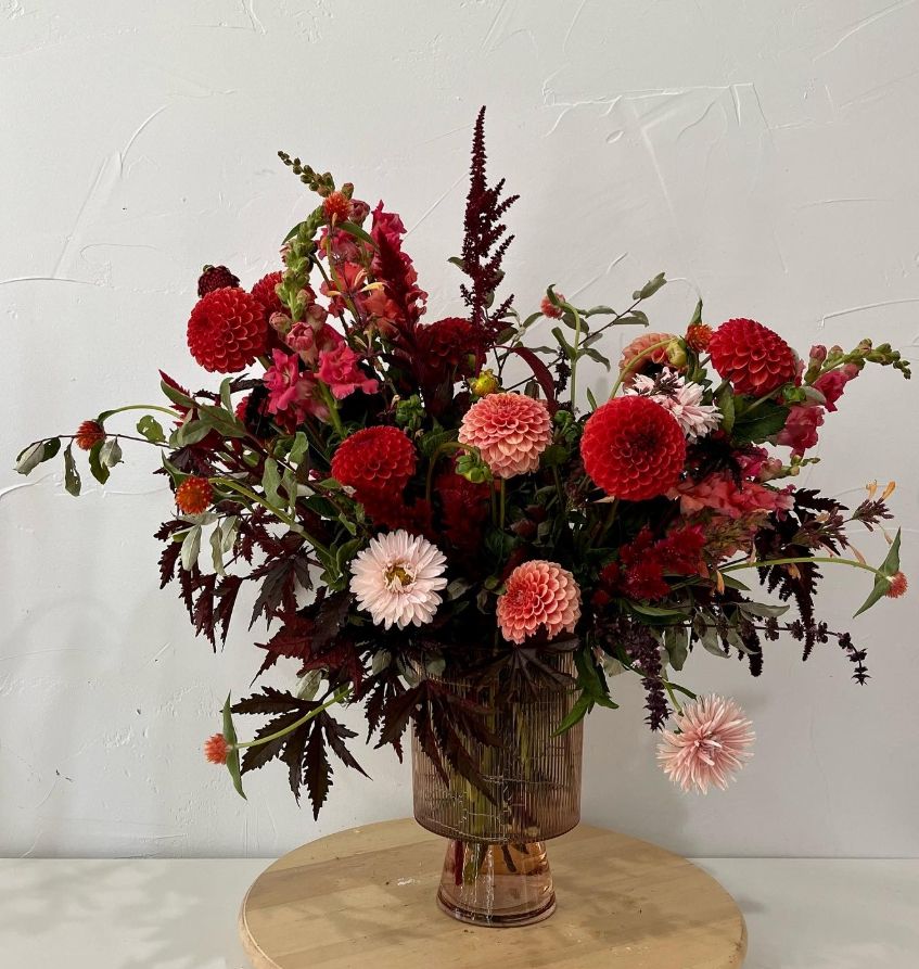 Dramatic red and burgundy floral arrangement with dahlias and roses in glass vase.