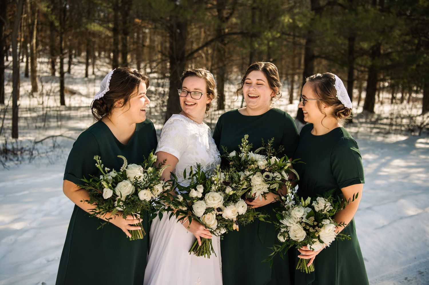 Wedding party in dark green dresses poses in snowy winter setting with white bouquets.