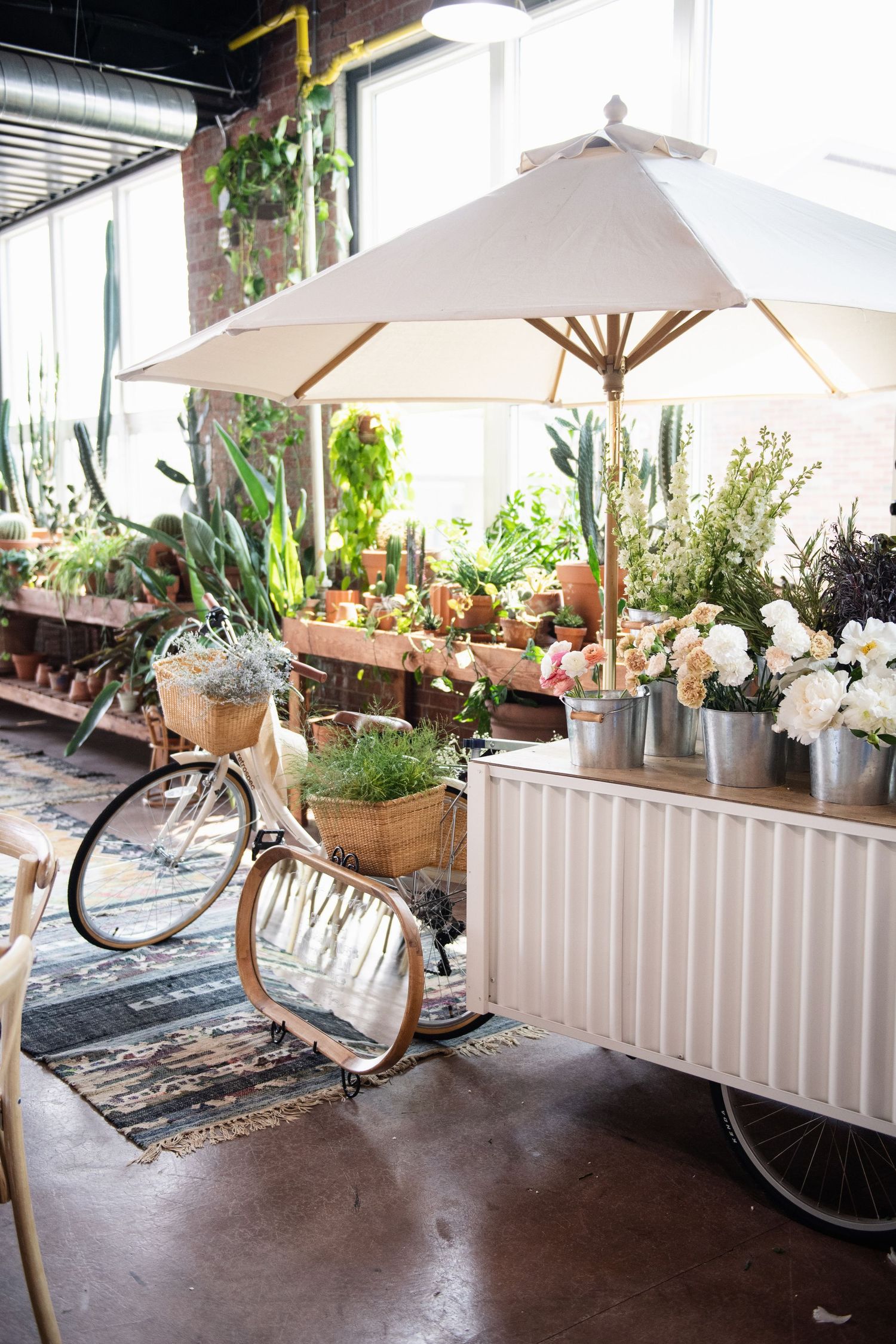 Rustic event space featuring vintage bicycle, potted plants, and white umbrella against exposed brick wall.