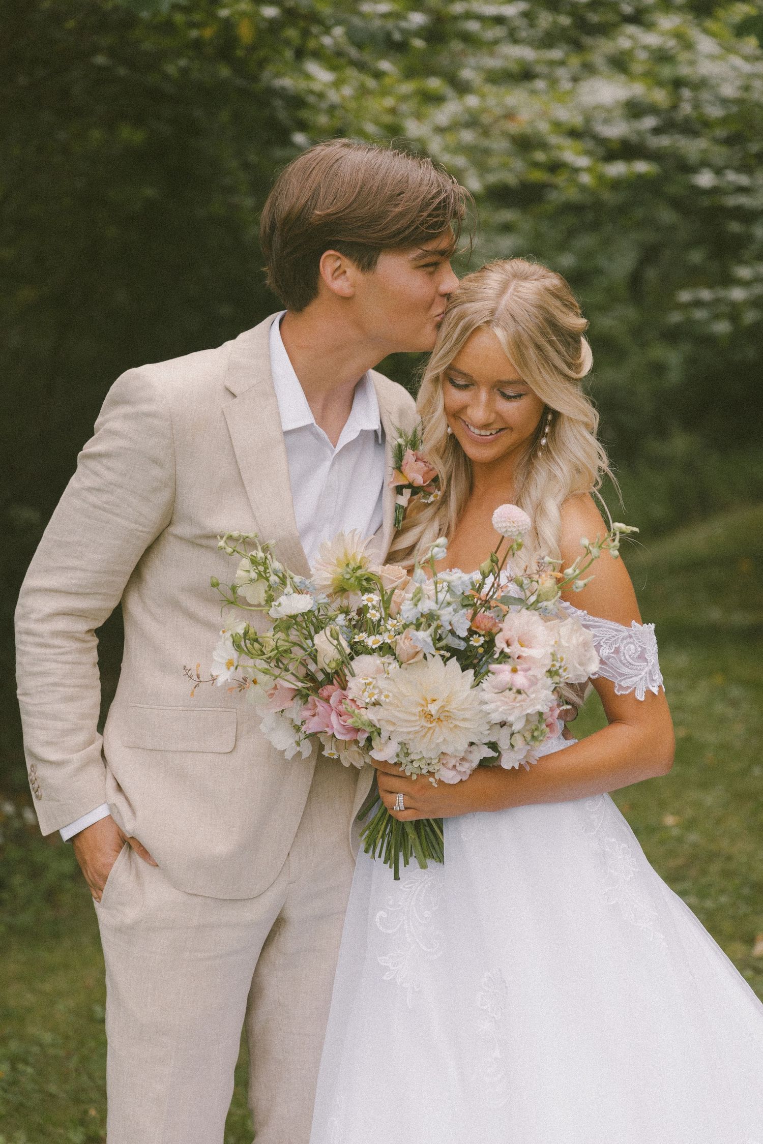 Romantic garden wedding portrait with couple in beige and white attire holding floral bouquet.