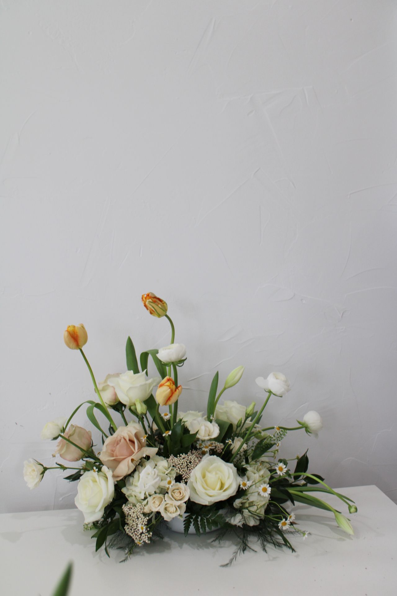 Low profile white and peach flower arrangement with tulips and roses against a gray background.