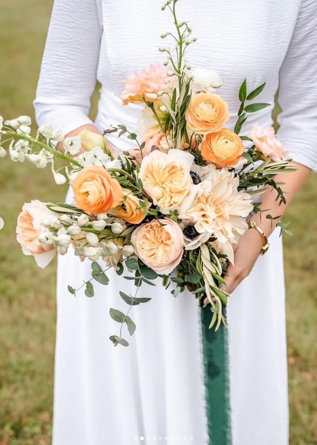 Elegant bridal bouquet featuring peachy roses, dahlias and eucalyptus against white dress.