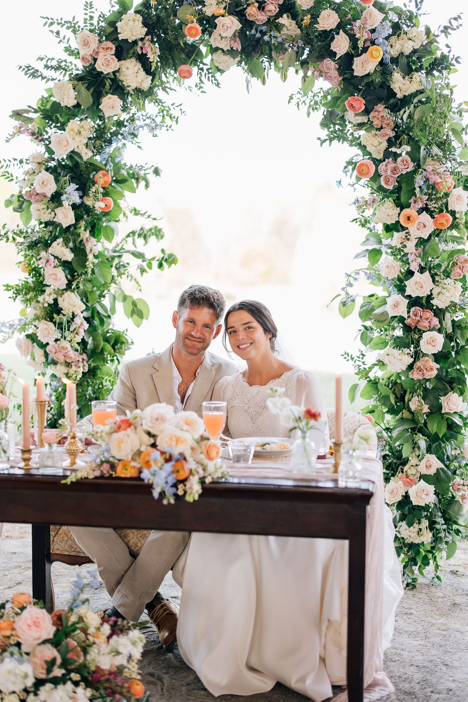 A romantic wedding reception table decorated with lush floral arches and pink roses in an elegant outdoor setting.