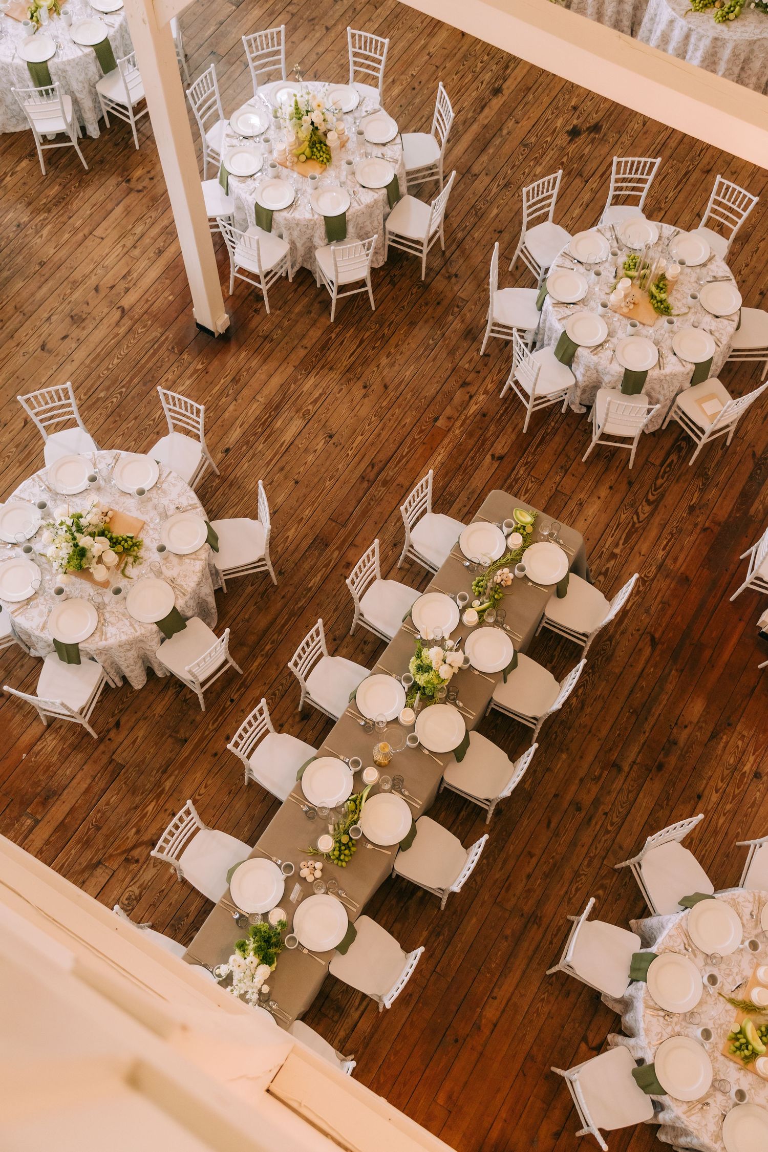 Overhead view of elegant wedding reception setup with white chairs and tables on hardwood floors.