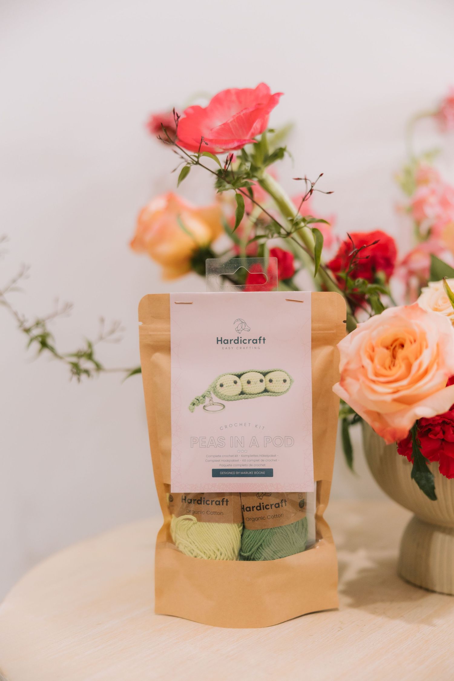 A kraft paper package of Hausdraft product sits beside a vase of pink and coral roses on a white surface.