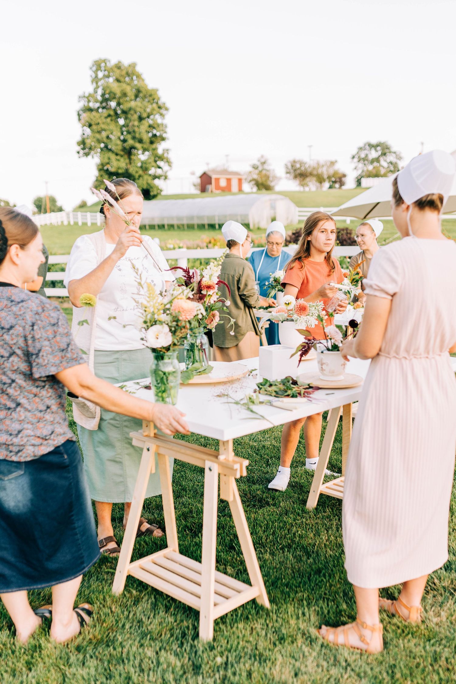 Group gathered around tables for an outdoor flower arranging workshop in a sunny garden.