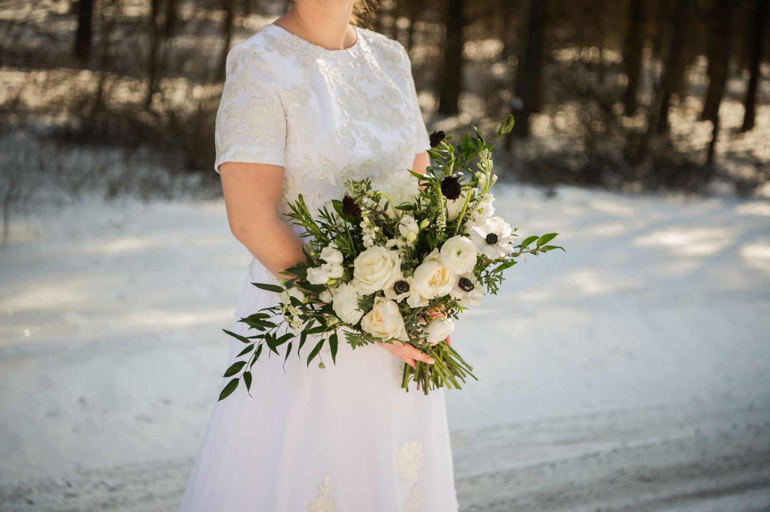 Close-up of white and green wedding bouquet held against a white wedding dress.