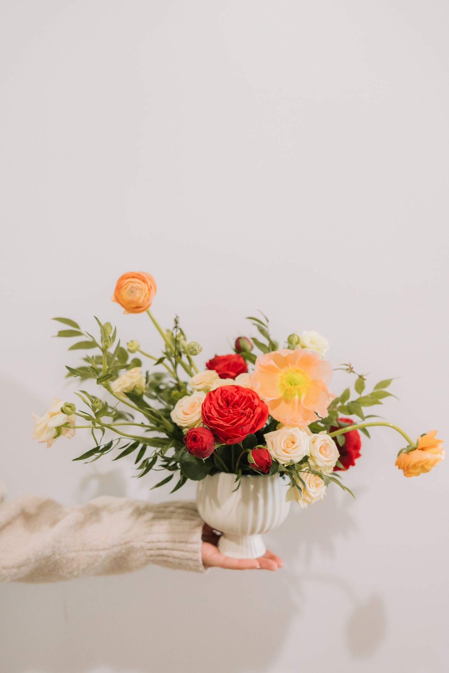 A delicate floral arrangement with red and peach blooms in white ceramic vases against a light gray background.