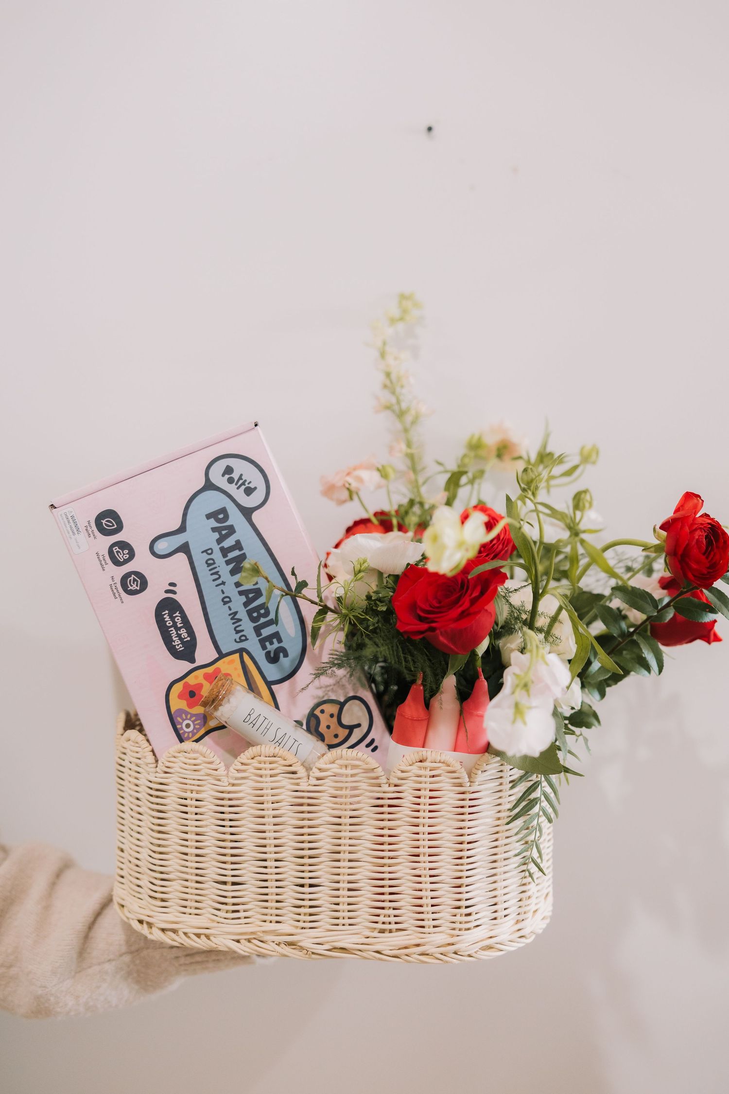 A white wicker basket filled with red and white flowers and a package of snacks against a light background.
