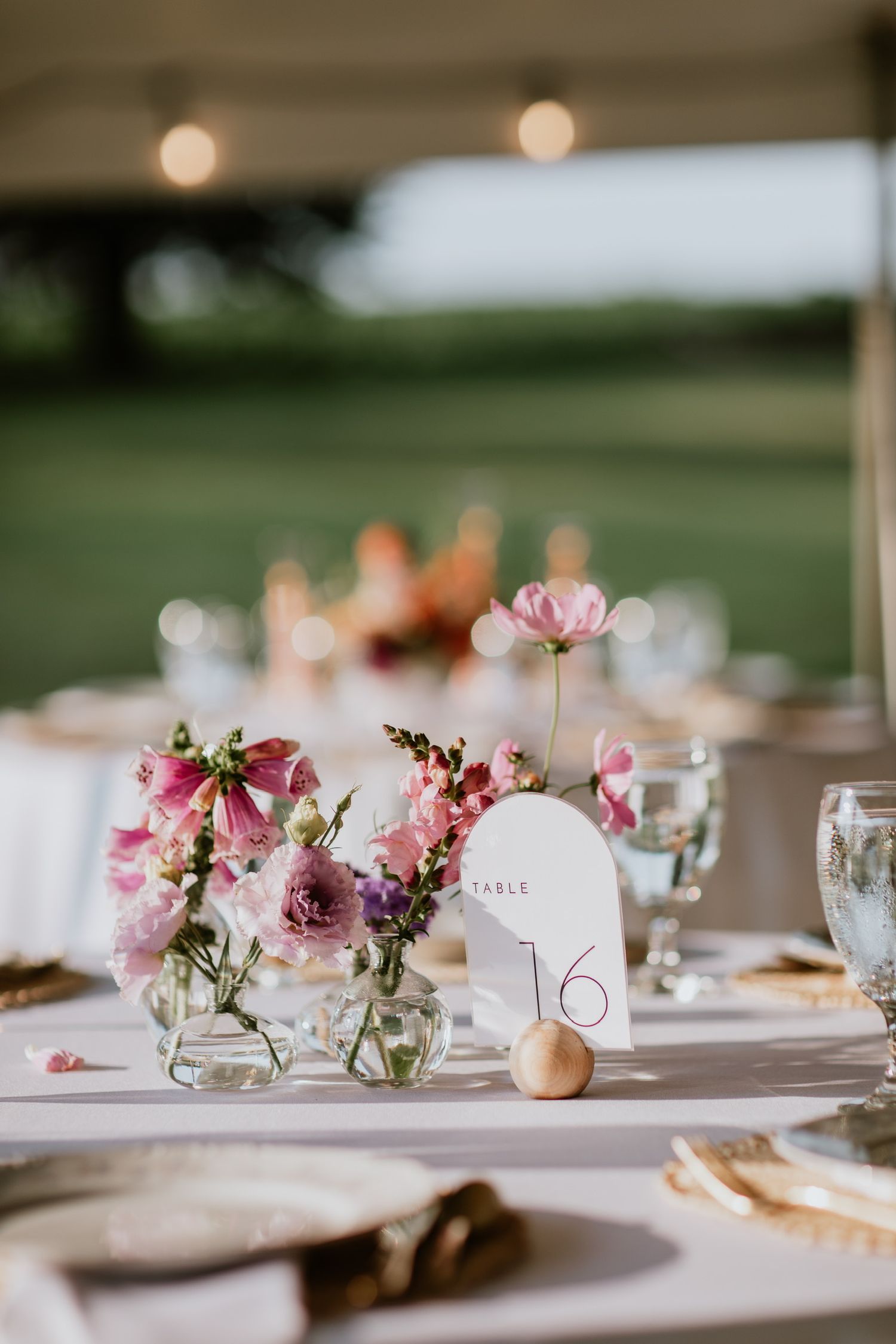 Delicate pink flowers in glass vases with table number 16 at elegant wedding place setting.