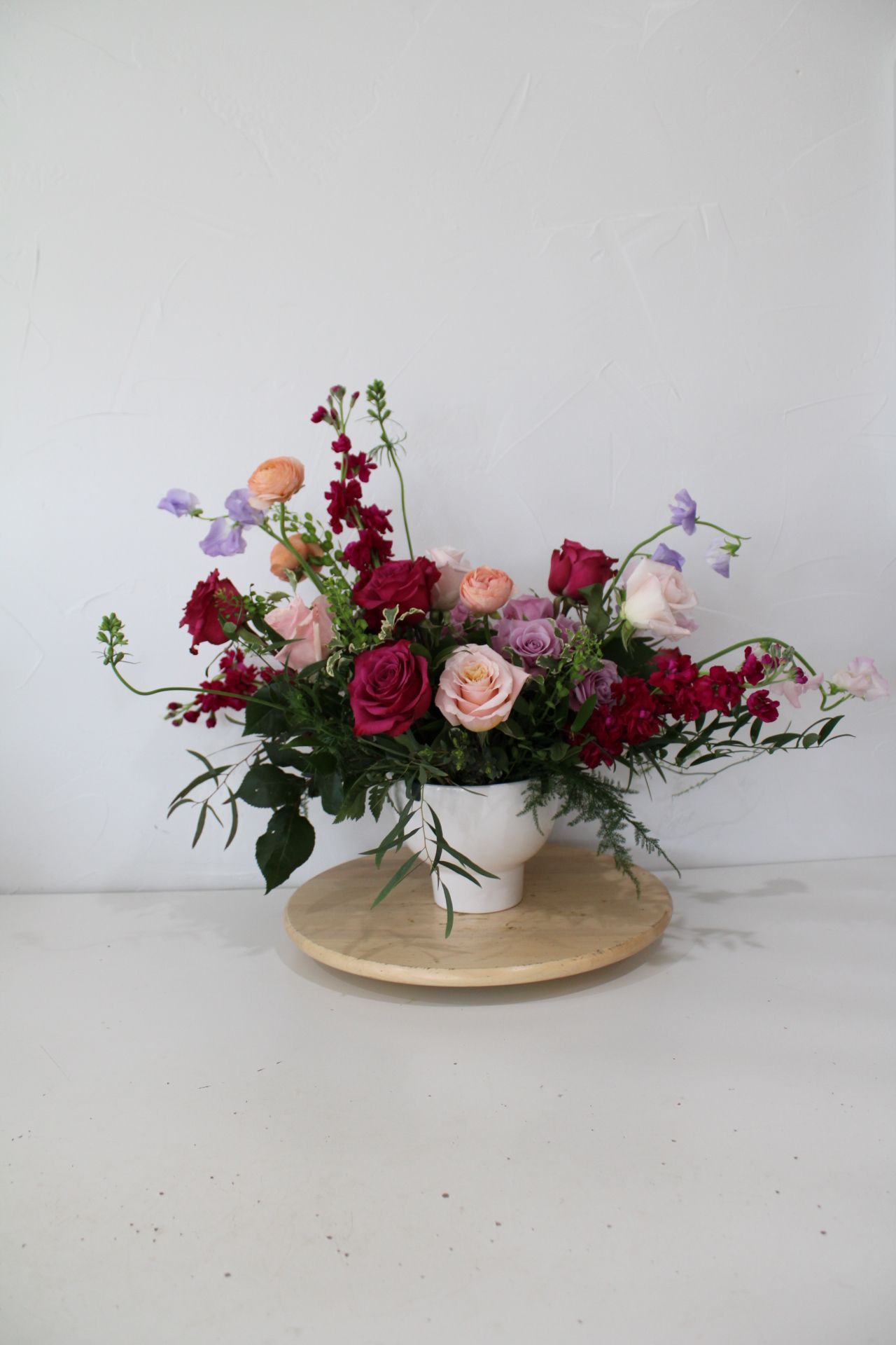 Deep red and pink roses arranged in a white ceramic bowl on a wooden base.